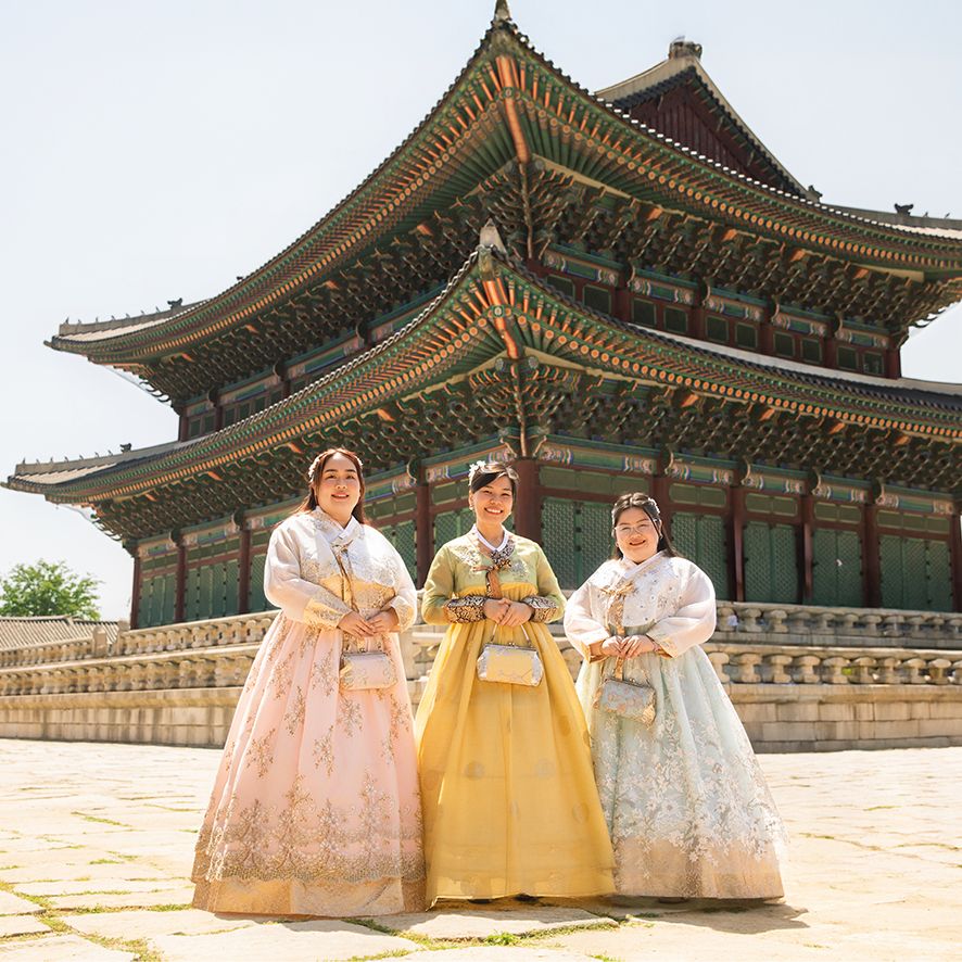 Traditional Korean palace buildings with ornate roofs and courtyards showcase women wearing vibrant hanbok dresses.