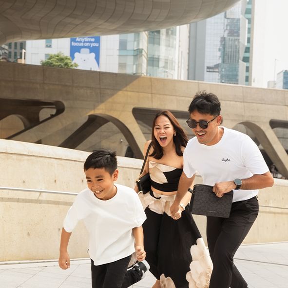 Group wearing white t-shirts and black pants jumping joyfully together in an urban setting near concrete architecture.