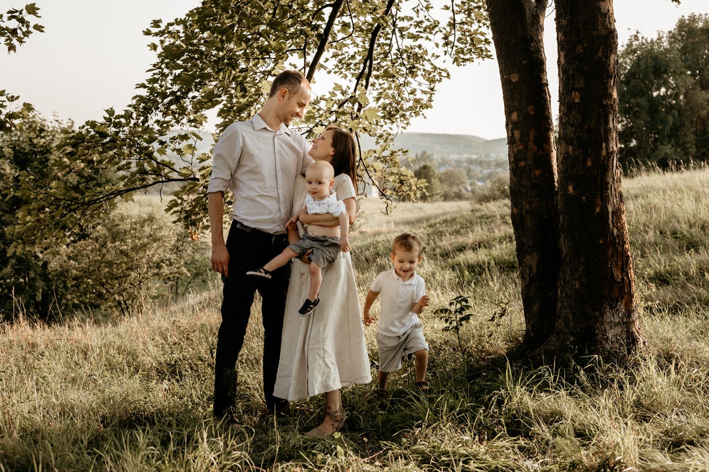 A couple and their child share tender moments together in an outdoor field during golden hour sunset.