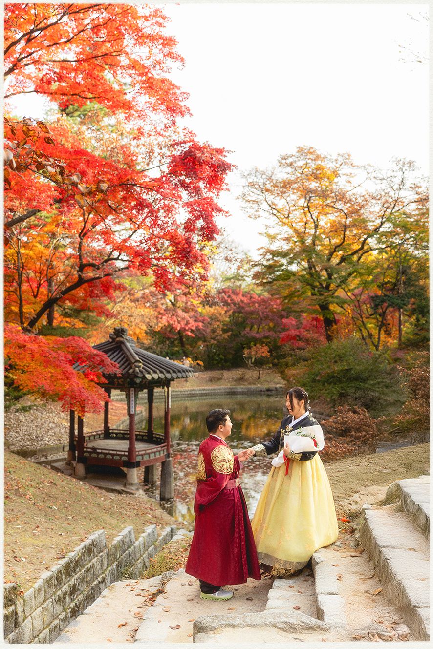Traditional Korean hanbok dresses create a vibrant contrast against autumn foliage at historic pavilion in Korea. Proposal Photoshoot Seoul