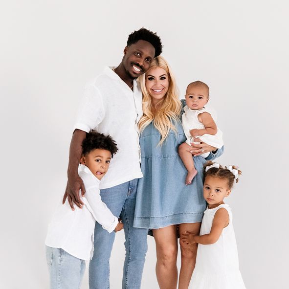Family in coordinated casual outfits of denim and white stand together in bright studio setting.