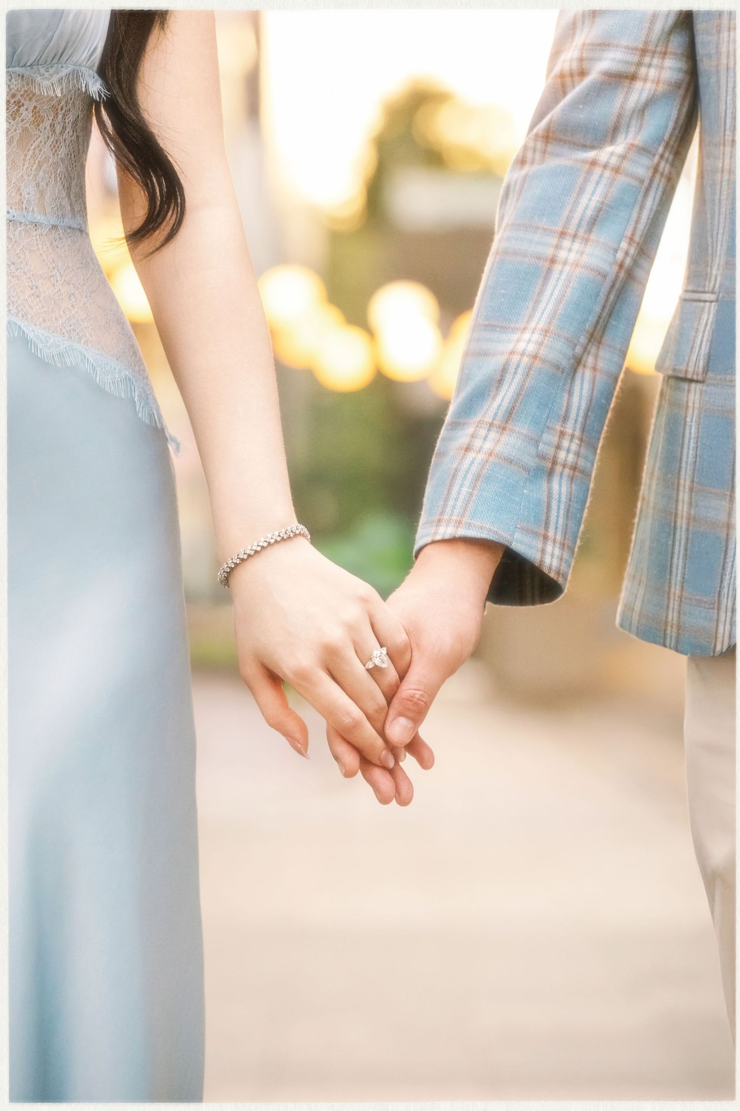 A couple holding hands outdoors in casual clothing during golden hour sunset lighting.
