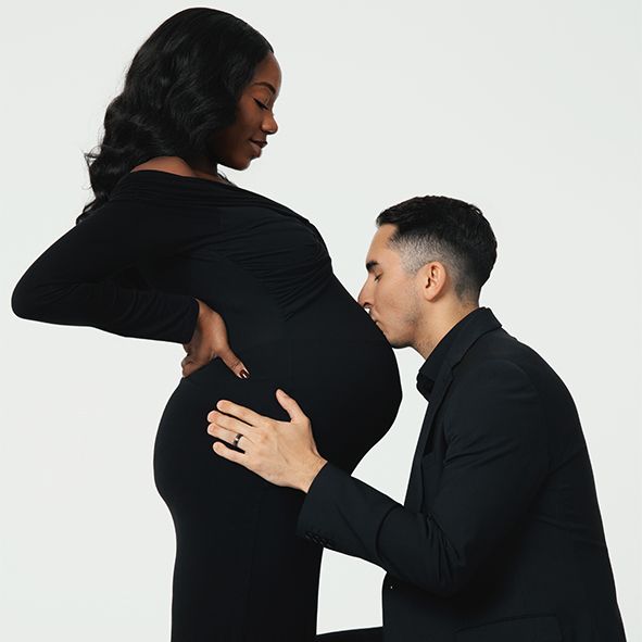 A pair dressed in black embracing while creating romantic silhouettes against a white studio backdrop.
