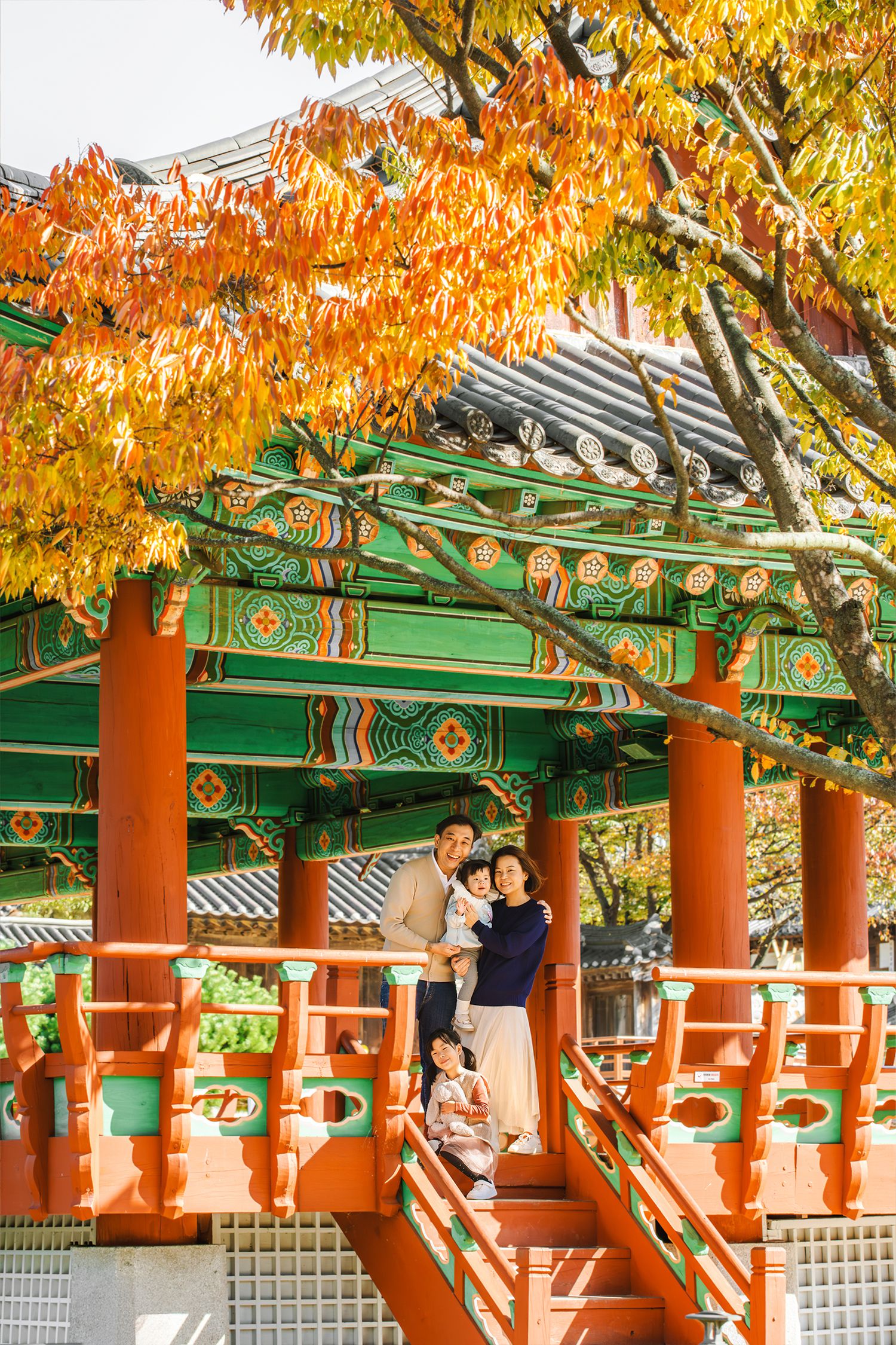 Traditional Korean temple pavilion with red pillars and ornate green roof details framed by vibrant autumn foliage.