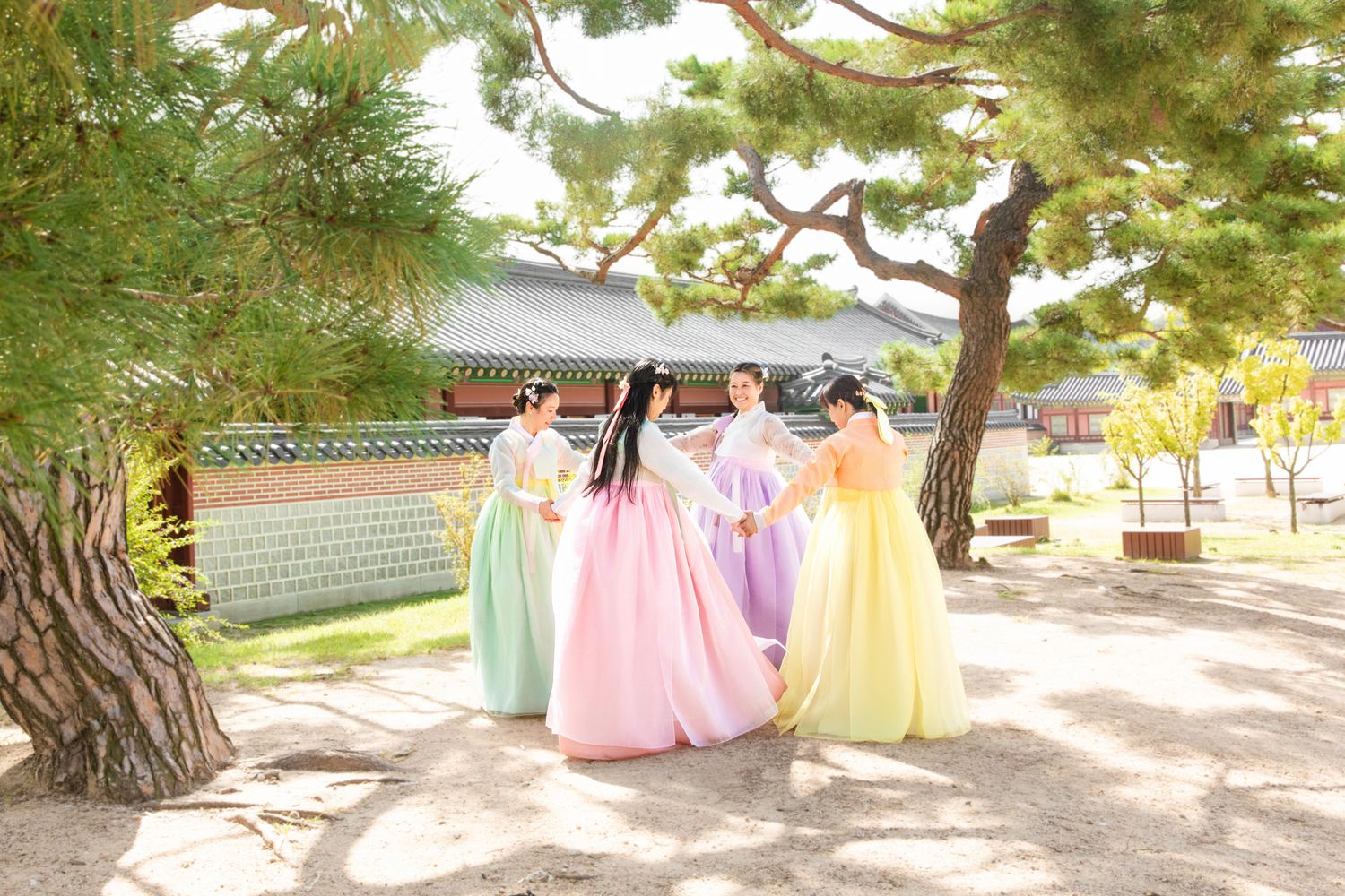 A collection of pastel colored bridesmaid dresses hanging from tree branches in an outdoor garden setting. Hanbok Photoshoot Seoul