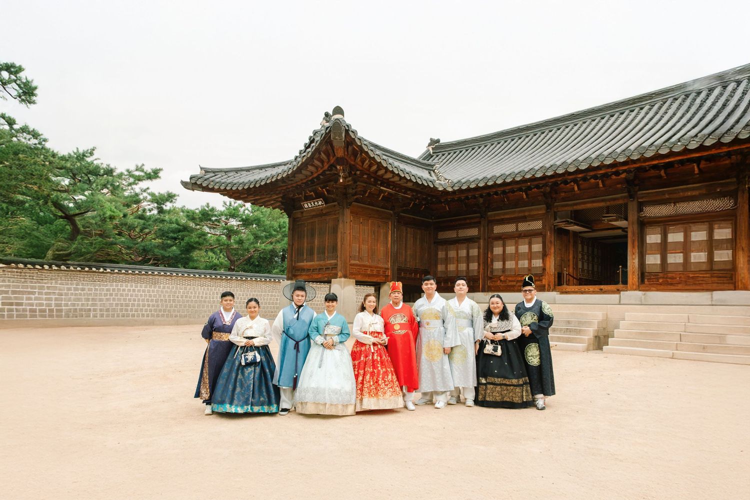 Traditional Korean palace courtyard with wooden buildings, ornate architecture, and stone paths on a sunny day.