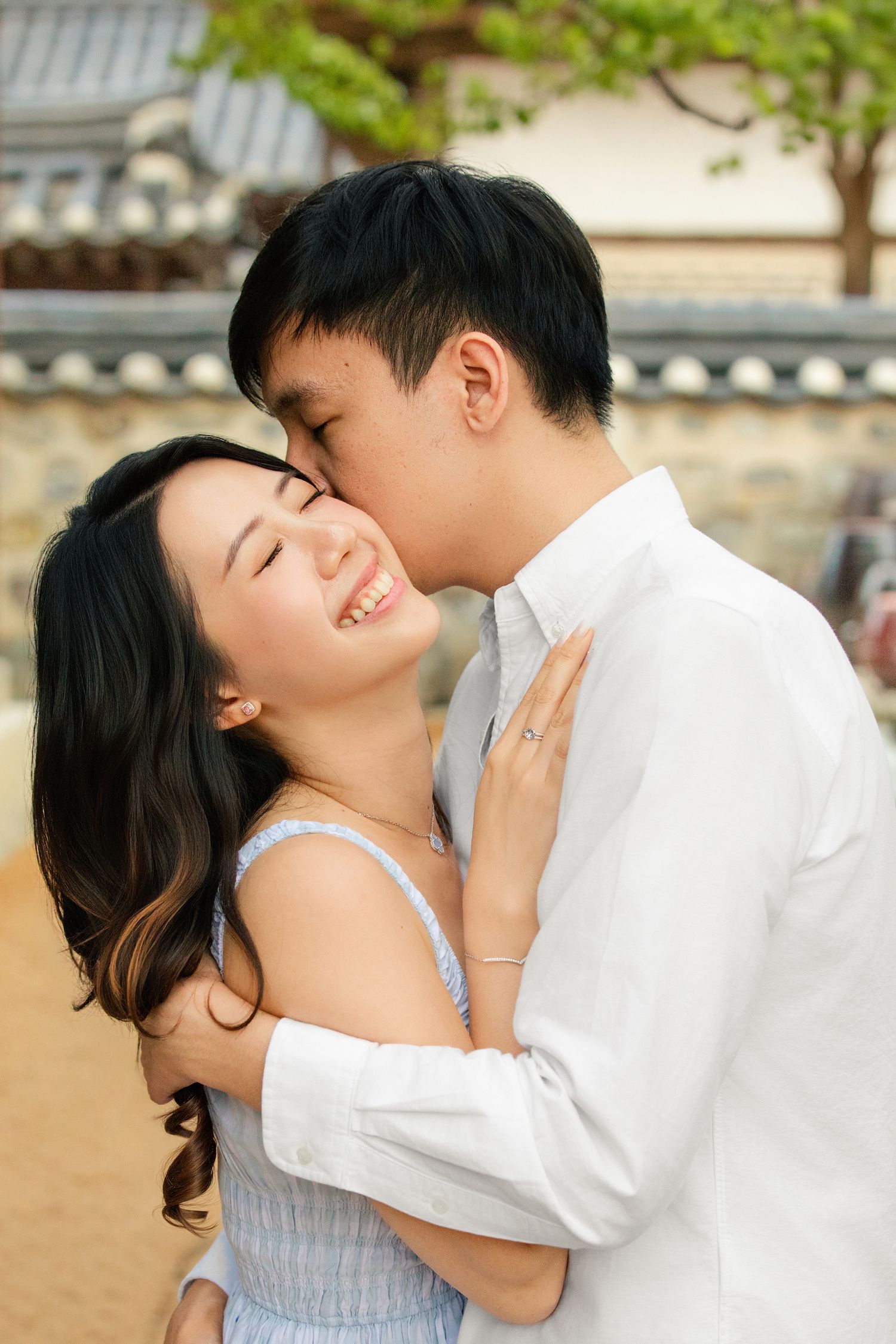 A romantic couple in white clothing share tender moments together outdoors against a traditional Asian architectural backdrop.