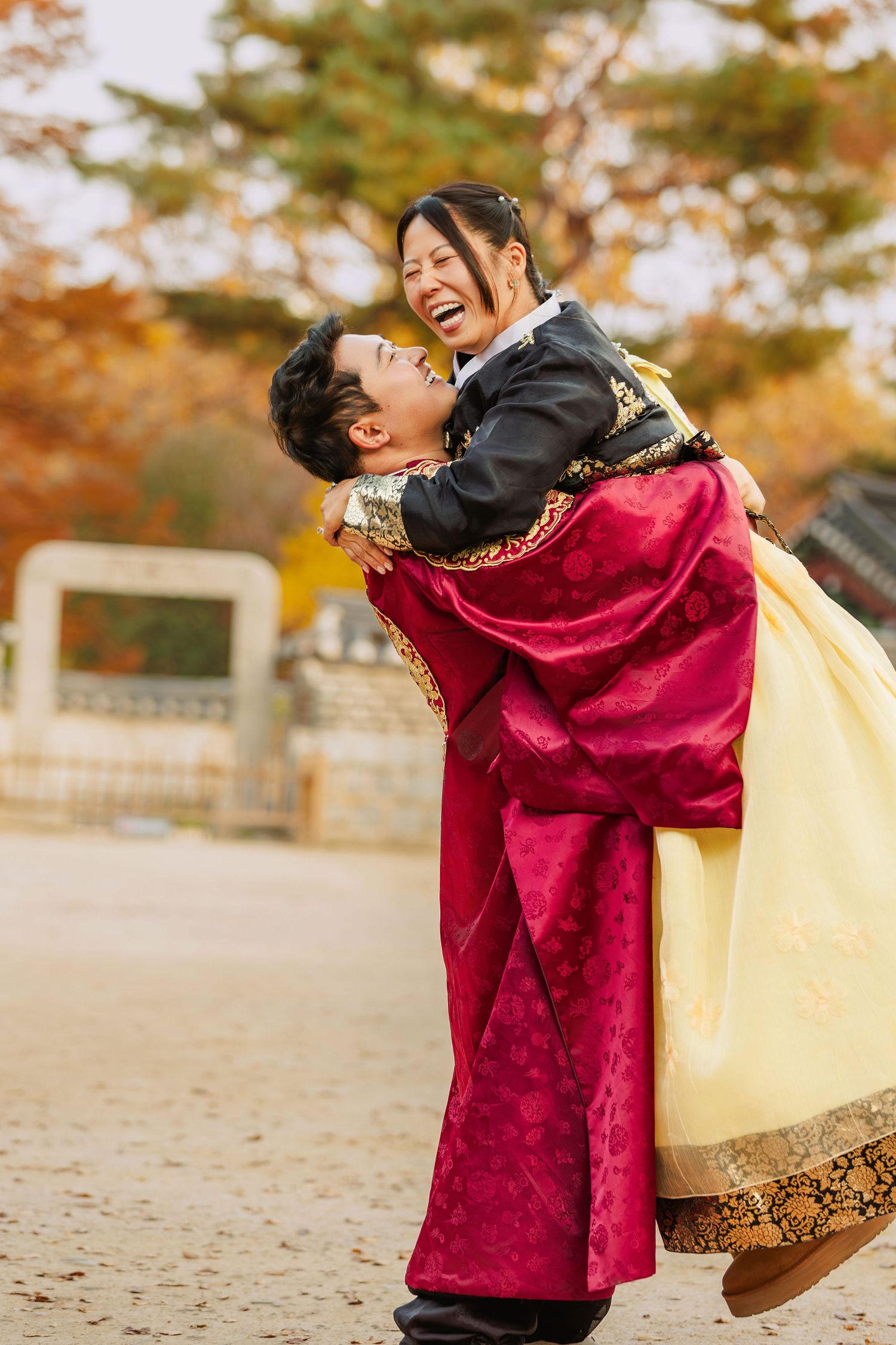 Couple in traditional Korean hanbok embracing and laughing joyfully outdoors in autumn.