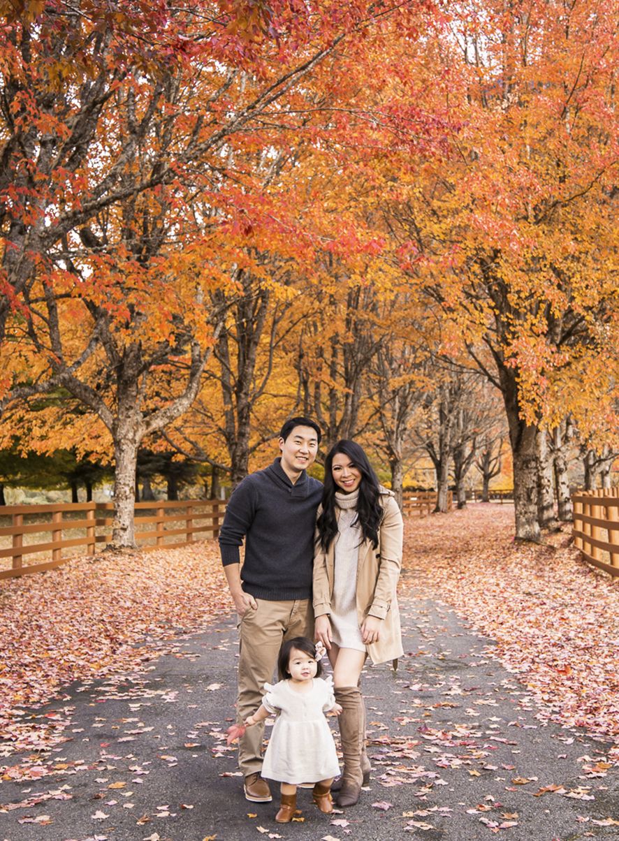 Family enjoying autumn scenery on a path lined with vibrant orange maple trees and fallen leaves.