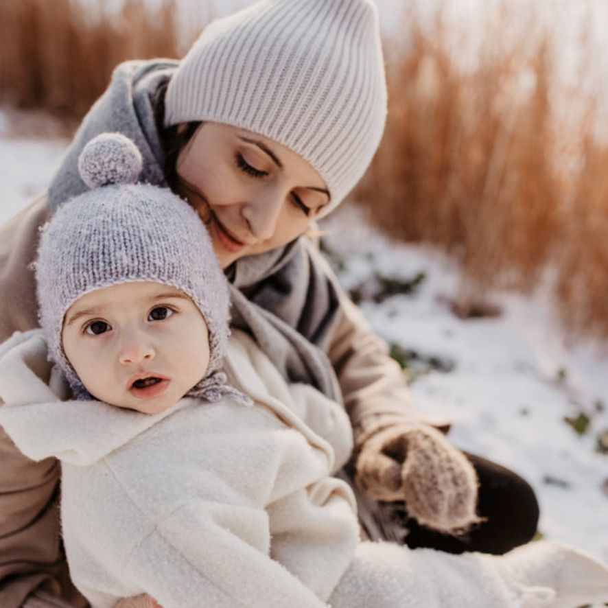 Cozy winter scene with two people in matching knit hats sitting together in the snow at sunset.