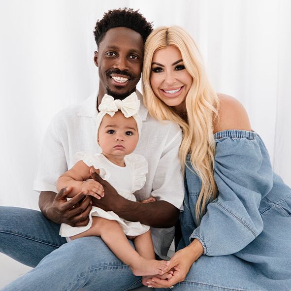 A happy interracial family with young baby sitting together and smiling against white background.