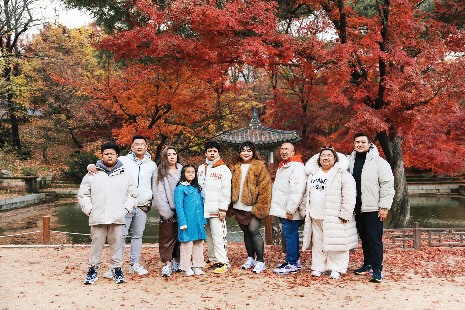 A group of people stand together for a photo under vibrant red autumn maple trees in a park.
