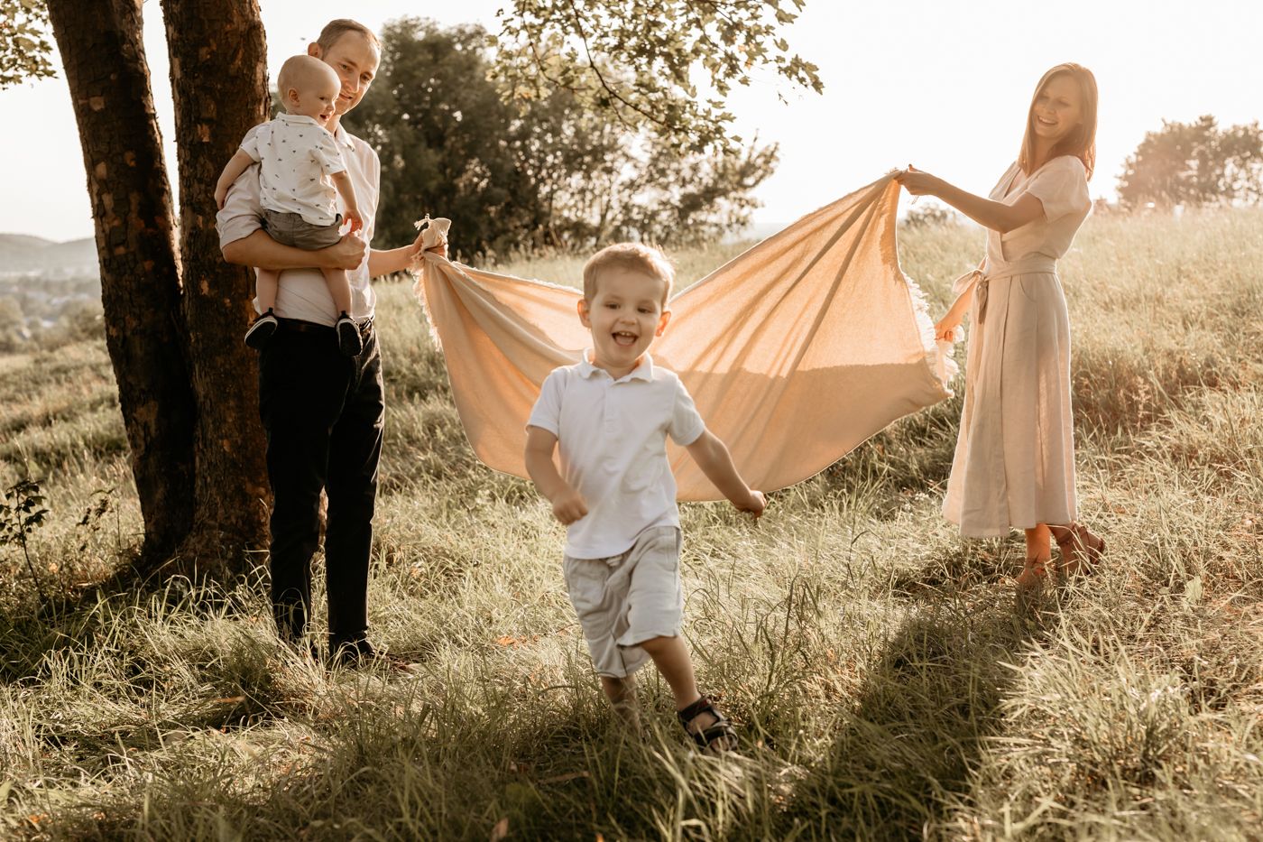 A joyous family moment captured at sunset in a field with a child running and flowing fabric creating a dreamy atmosphere.