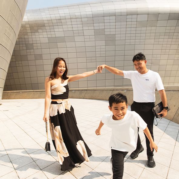 Three people in coordinated black and white outfits pose playfully at a modern architectural site with curved walls.