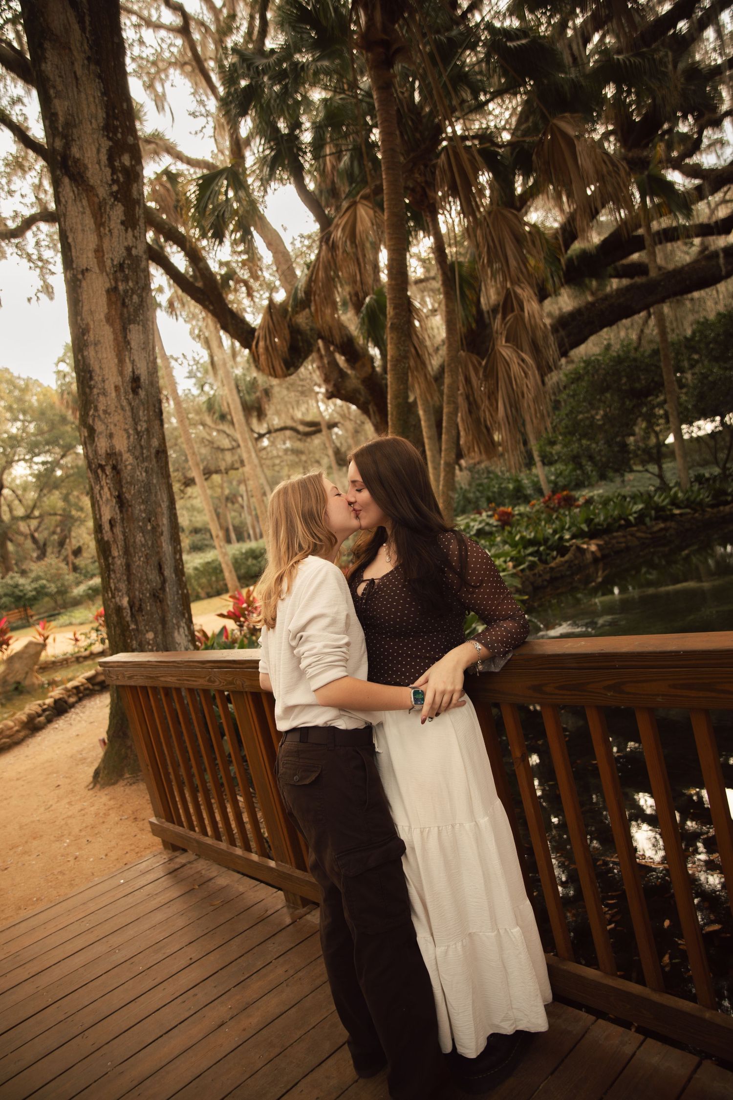 A couple shares a romantic moment on a wooden deck surrounded by towering eucalyptus trees at sunset.