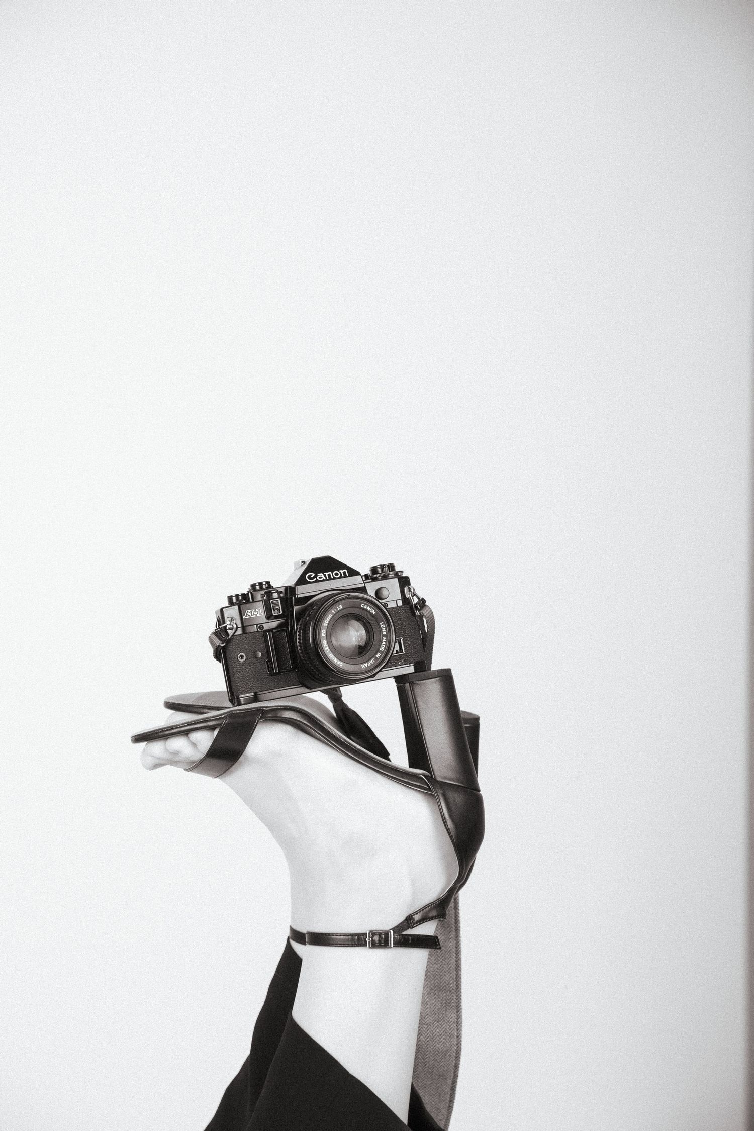 Vintage camera with leather strap photographed in black and white against a white background.