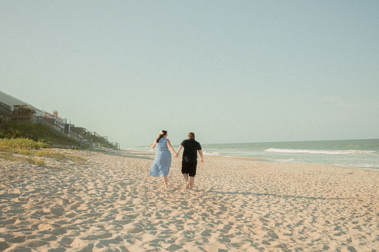 A serene empty beach stretches into the distance under a bright sky.