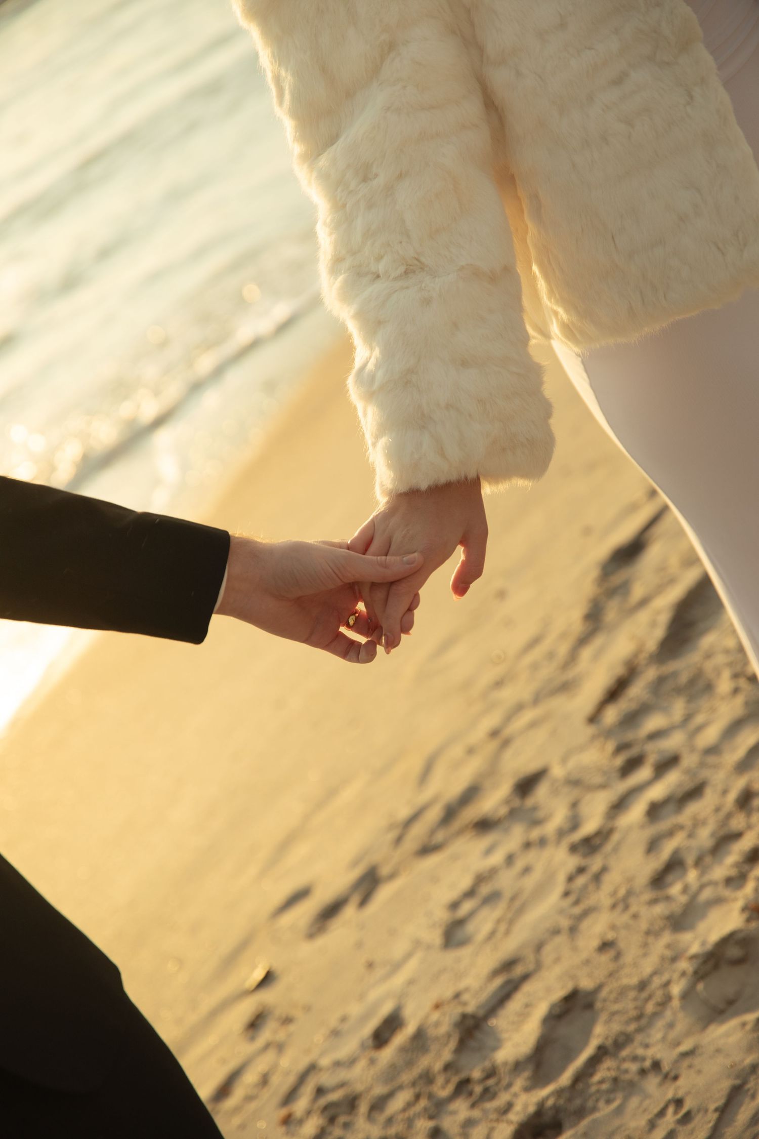 Two hands reaching to hold each other against a golden sunset on a snowy winter landscape.