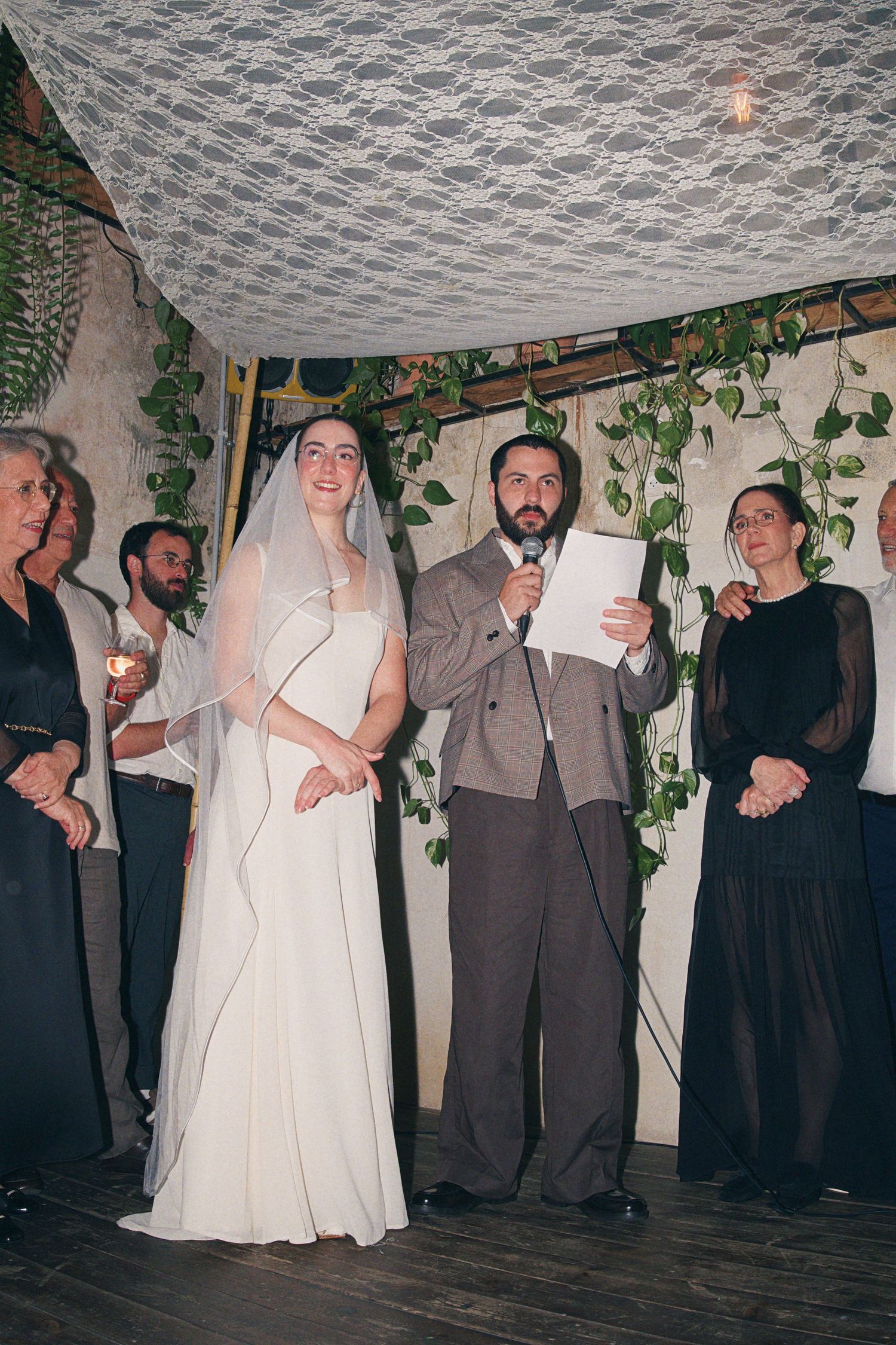 Bride in veil and groom in plaid suit during wedding ceremony under chuppah.