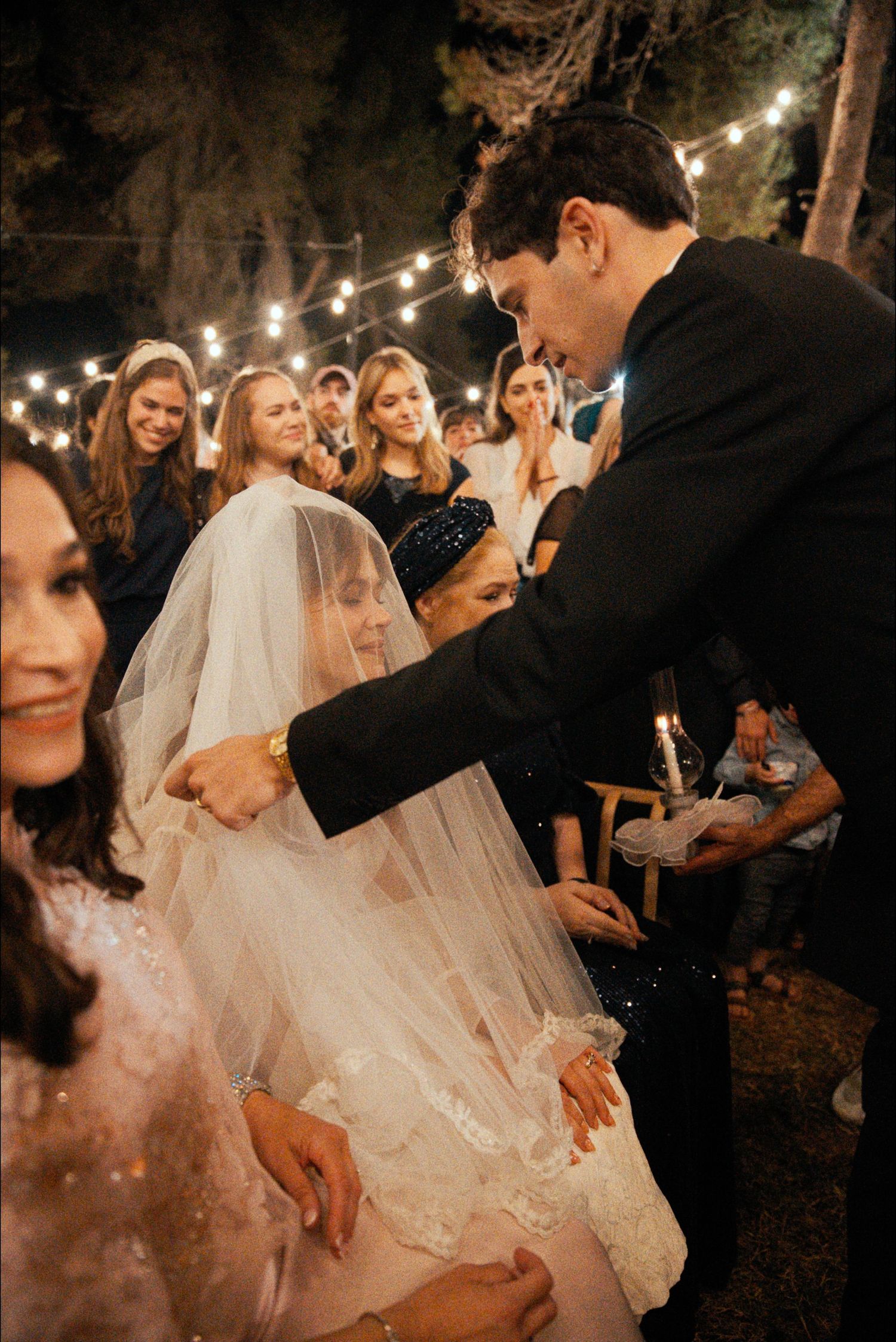 A couple shares a romantic dance moment under twinkling lights at their outdoor wedding celebration.