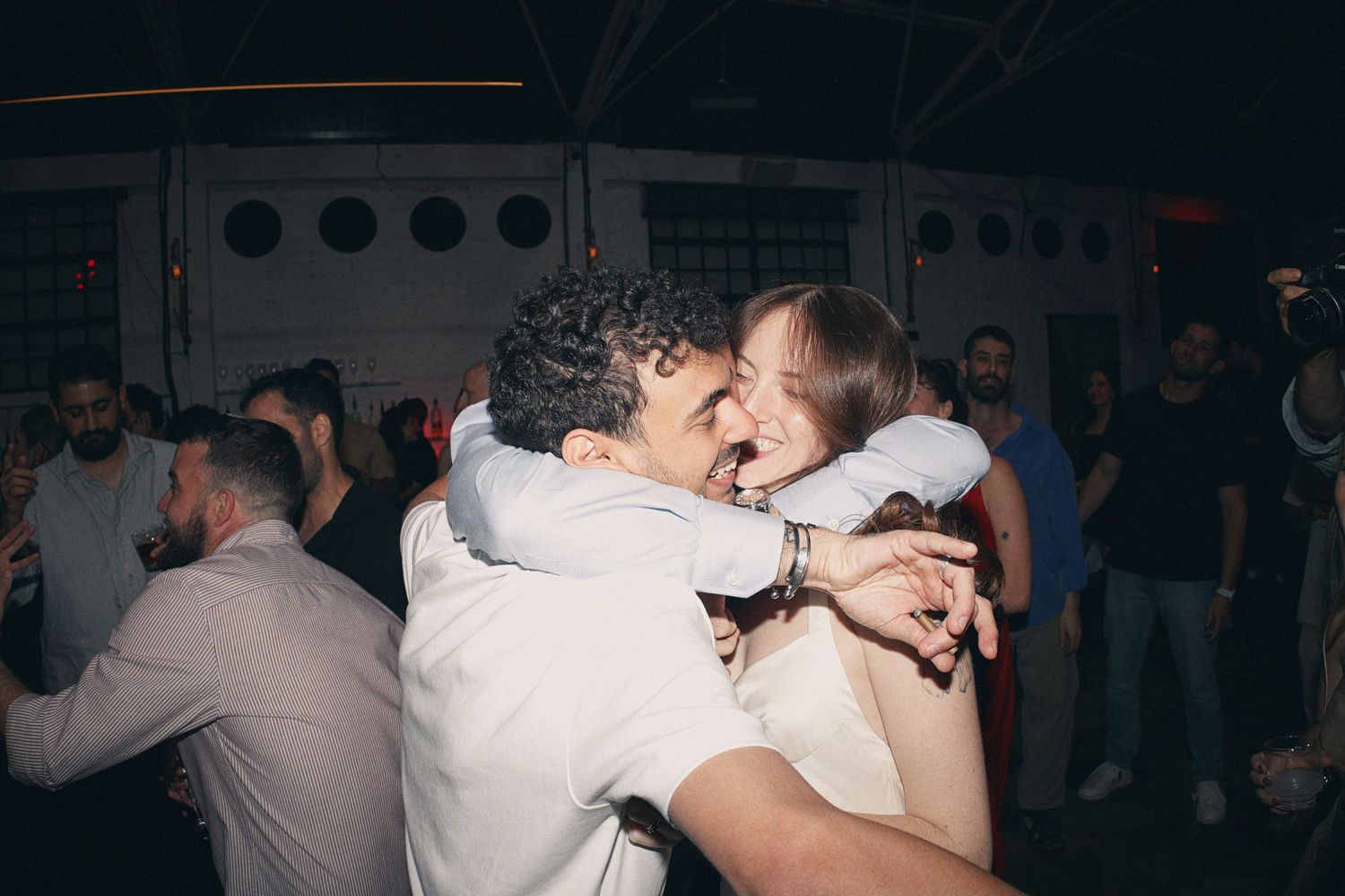 Two people share a joyful hug on a lively dance floor at a party or wedding reception.