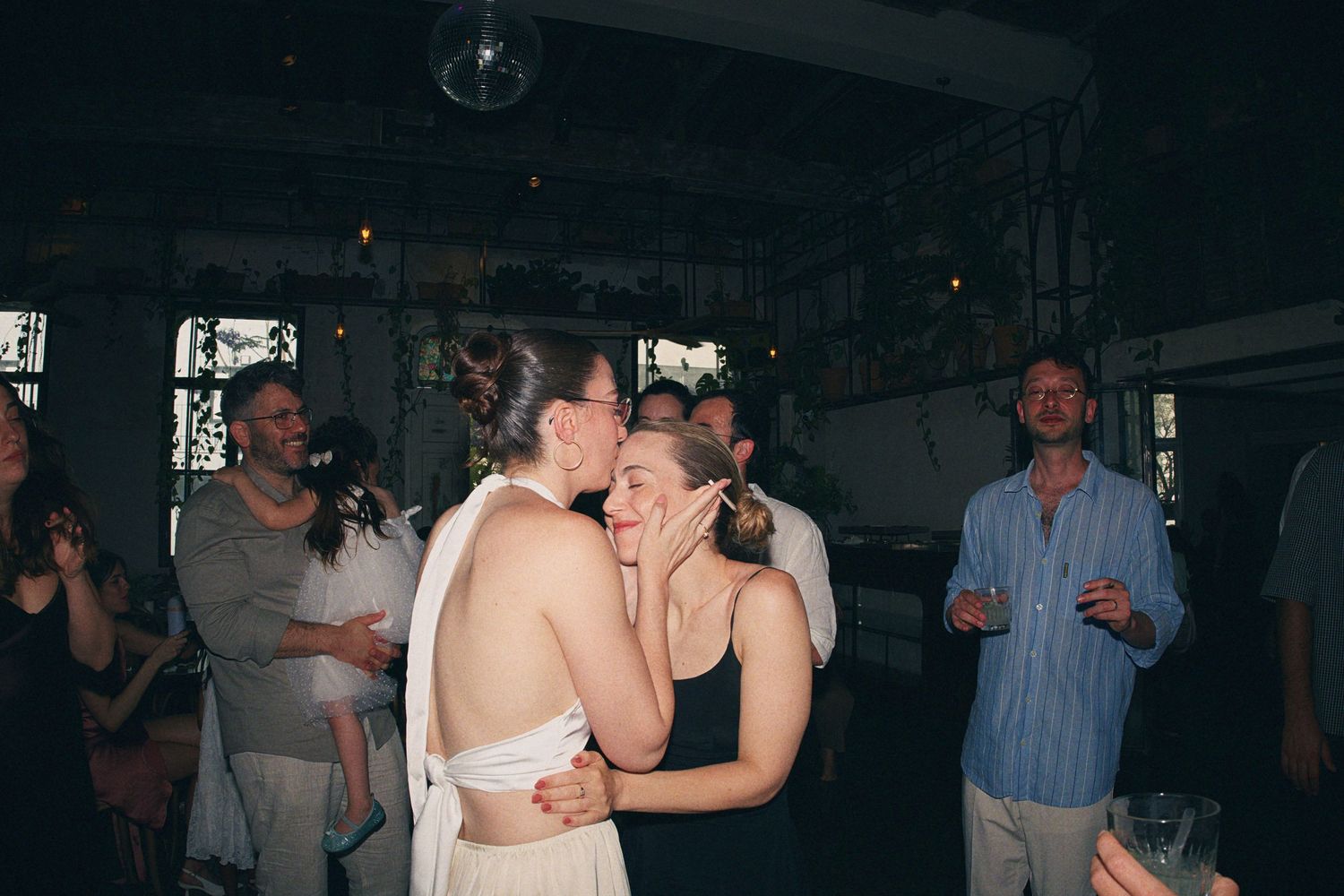Newlywed couple shares a kiss on the dance floor surrounded by celebrating wedding guests.
