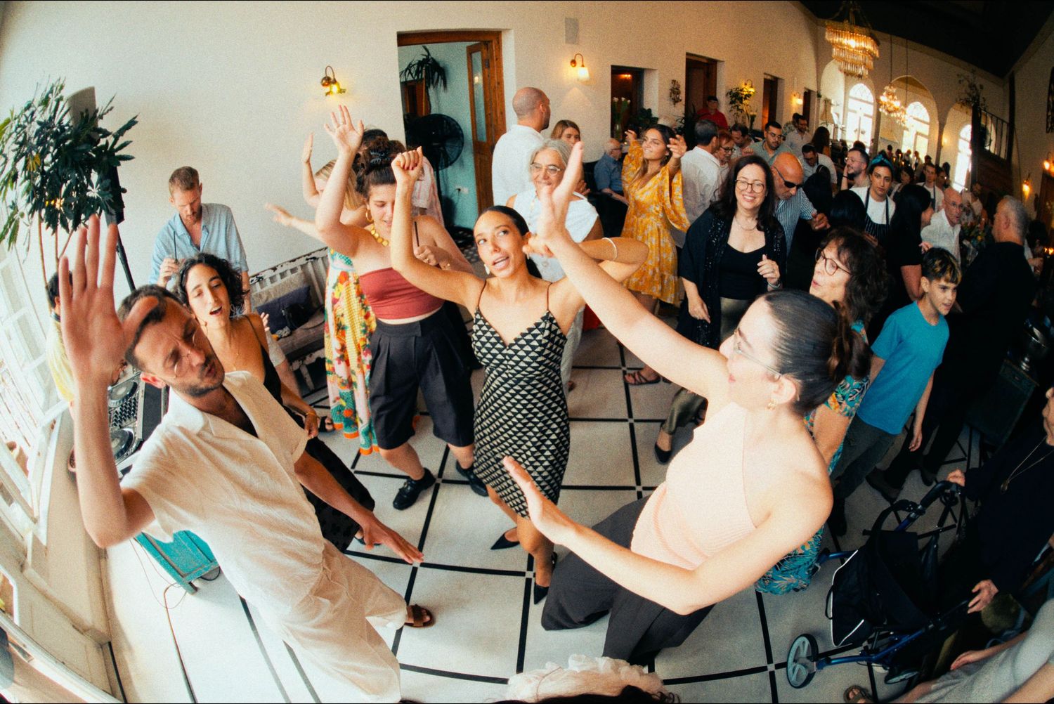 Wedding guests dance enthusiastically at a lively indoor reception.
