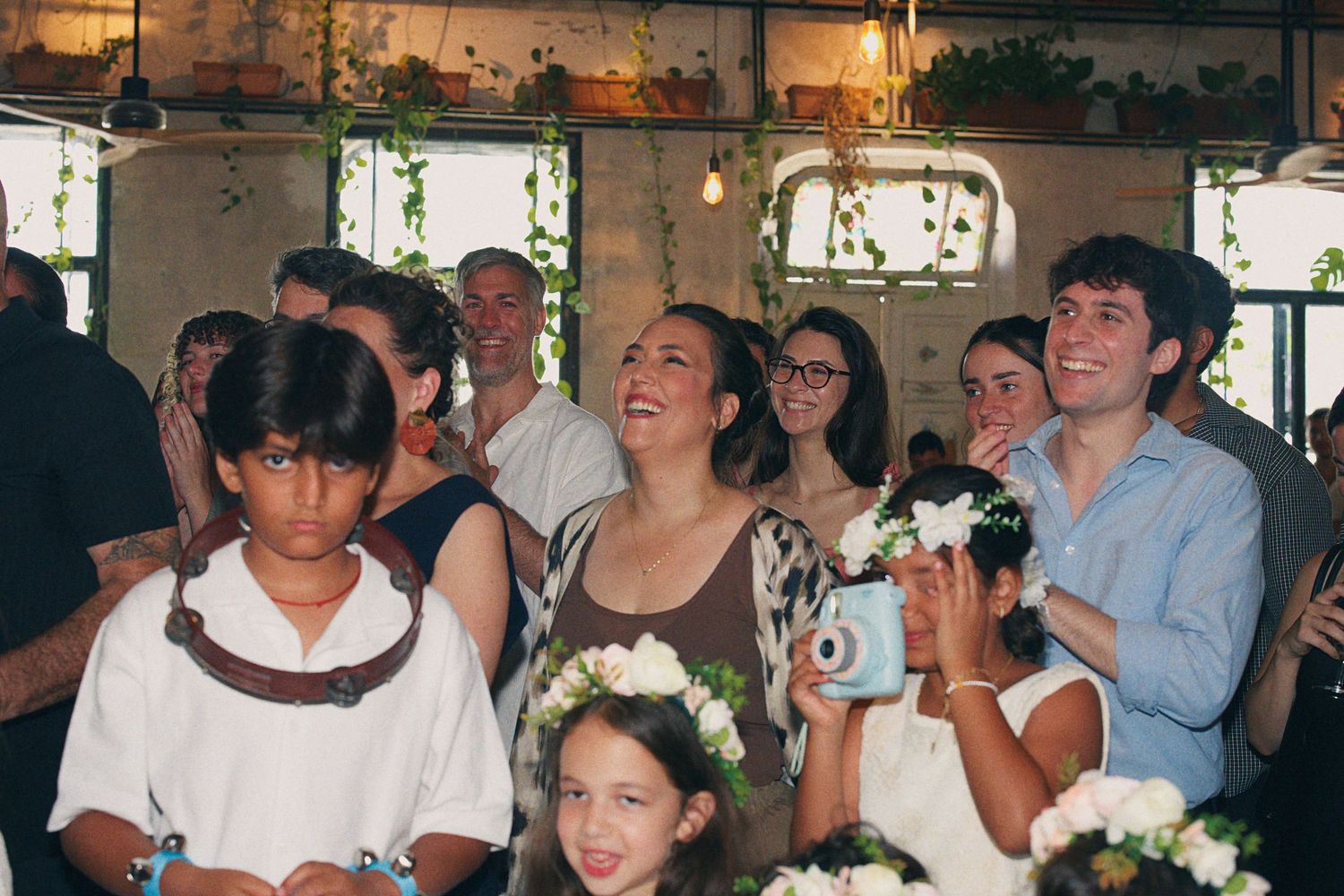 Guests smiling and laughing at a wedding reception, including flower girls wearing floral crowns.