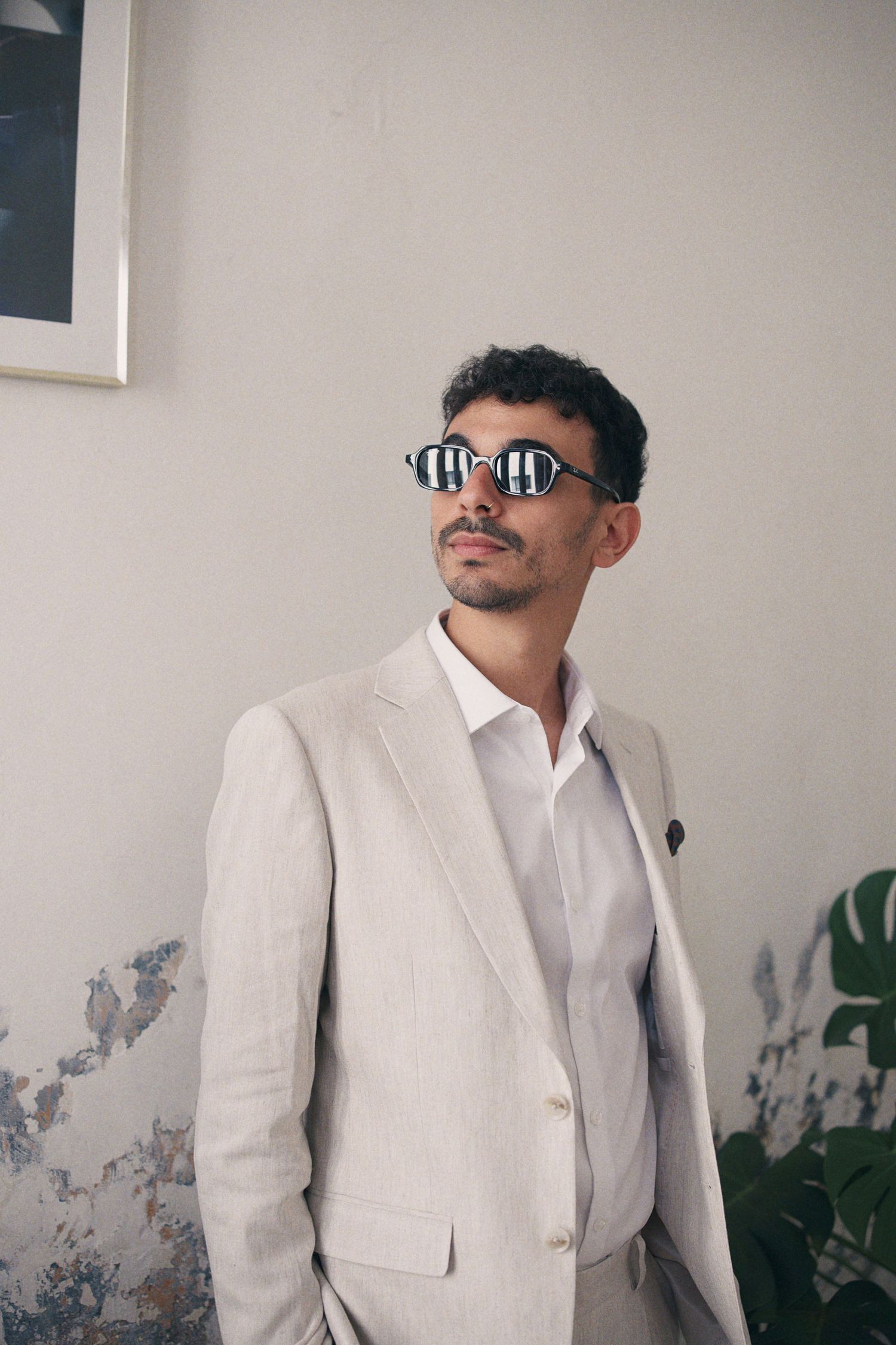 Stylish man in a linen suit wearing bold striped sunglasses posing against a white wall.