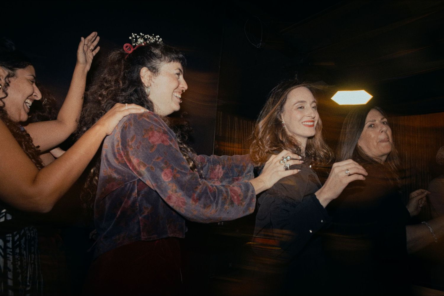 Party guests dancing with raised arms in a dimly lit venue with string lights overhead.