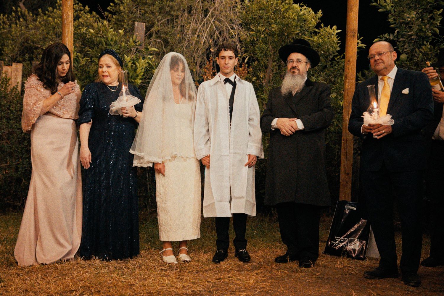 Wedding guests gather for a group photo at an outdoor evening celebration.