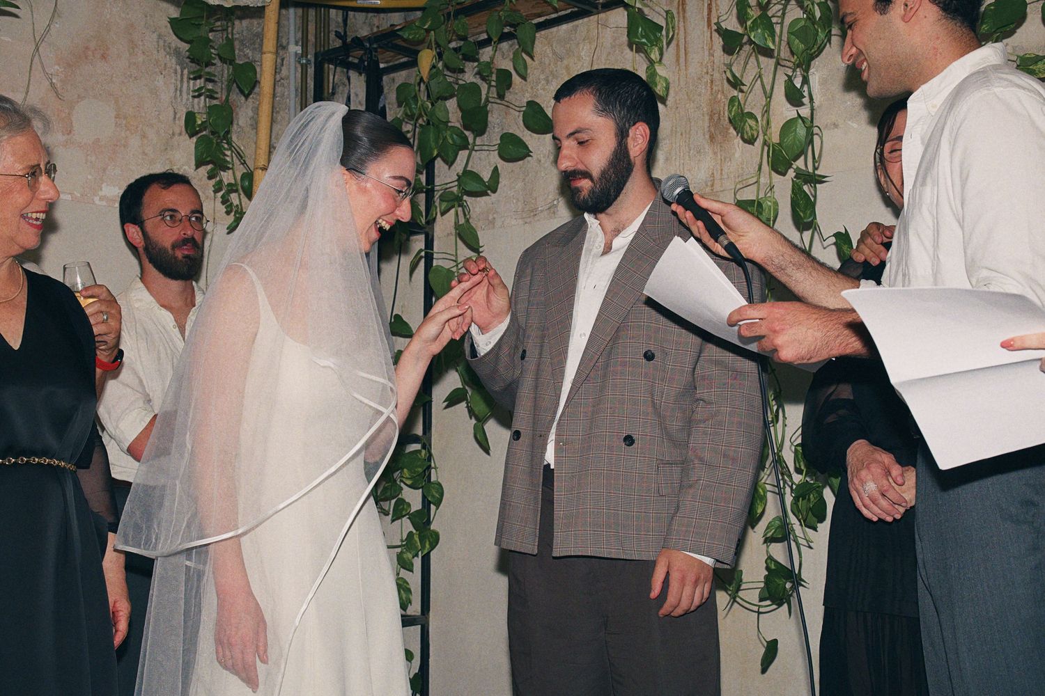Bride in white veil and groom in gray suit during outdoor Jewish wedding ring exchange.