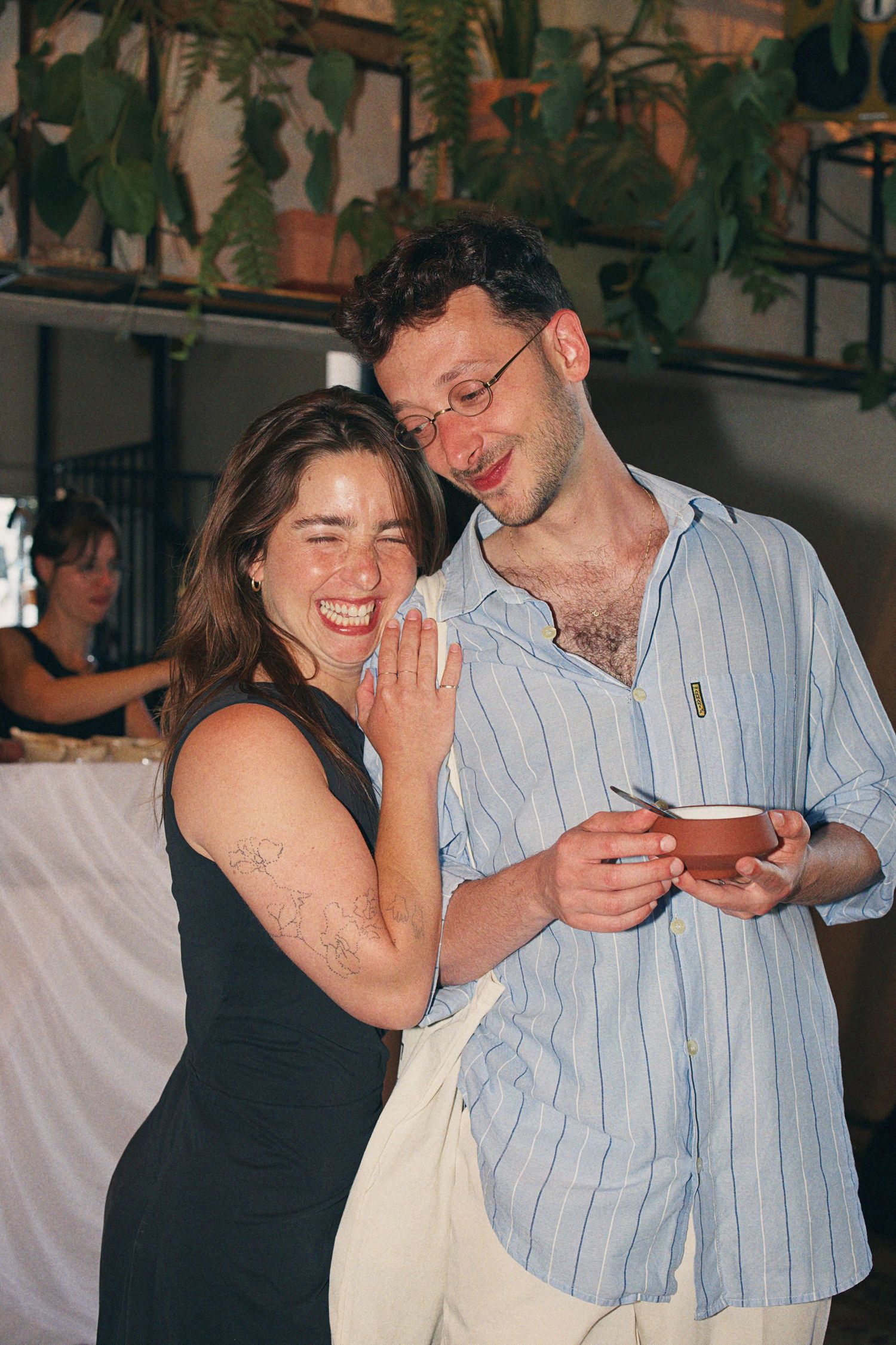 Smiling couple at wedding reception, woman in black dress and man in blue striped shirt.