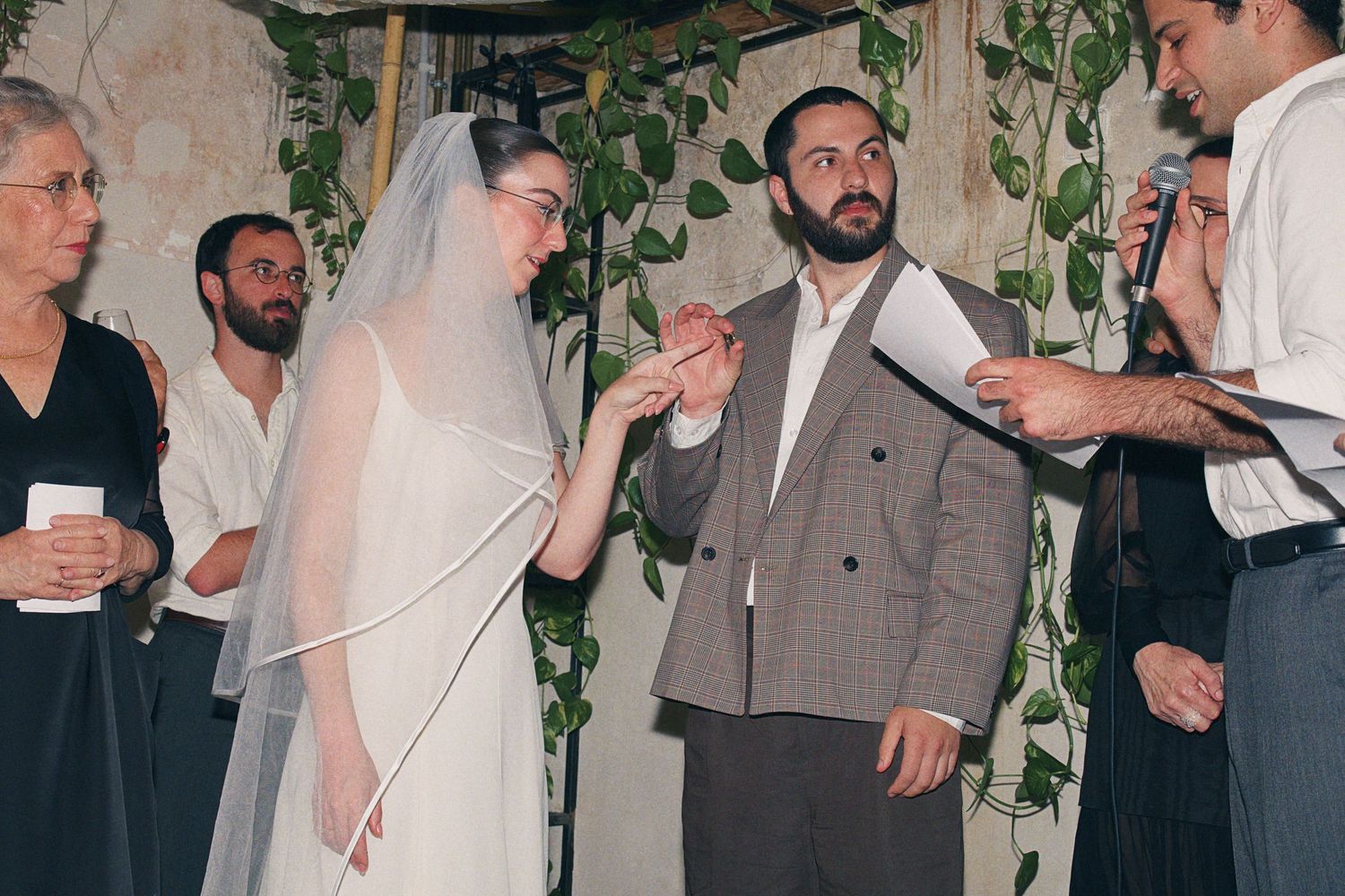 Bride and groom exchange rings under floral chuppah during Jewish wedding ceremony.