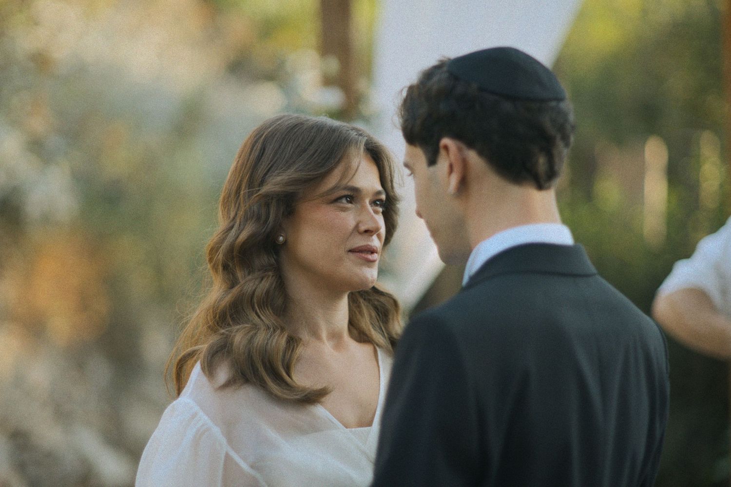Couple in wedding attire standing together outdoors during golden hour.