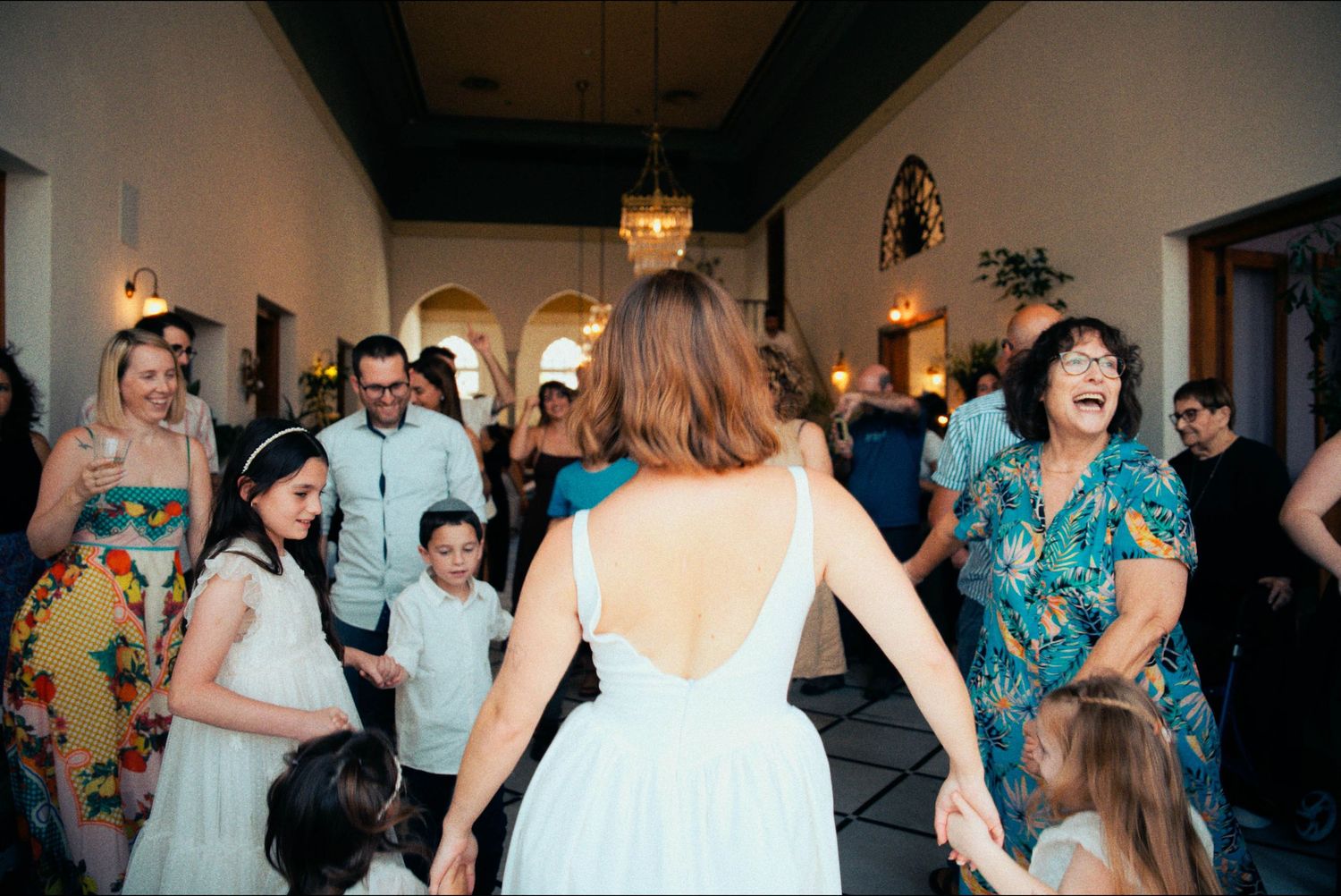 Wedding guests dance and celebrate in an elegant venue with arched doorways.