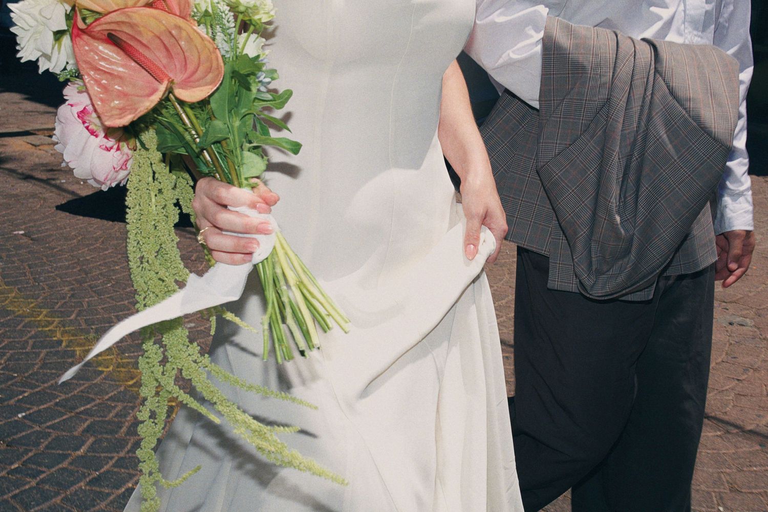 Bride in white gown holding tropical anthurium wedding bouquet with groom in gray suit outdoors.