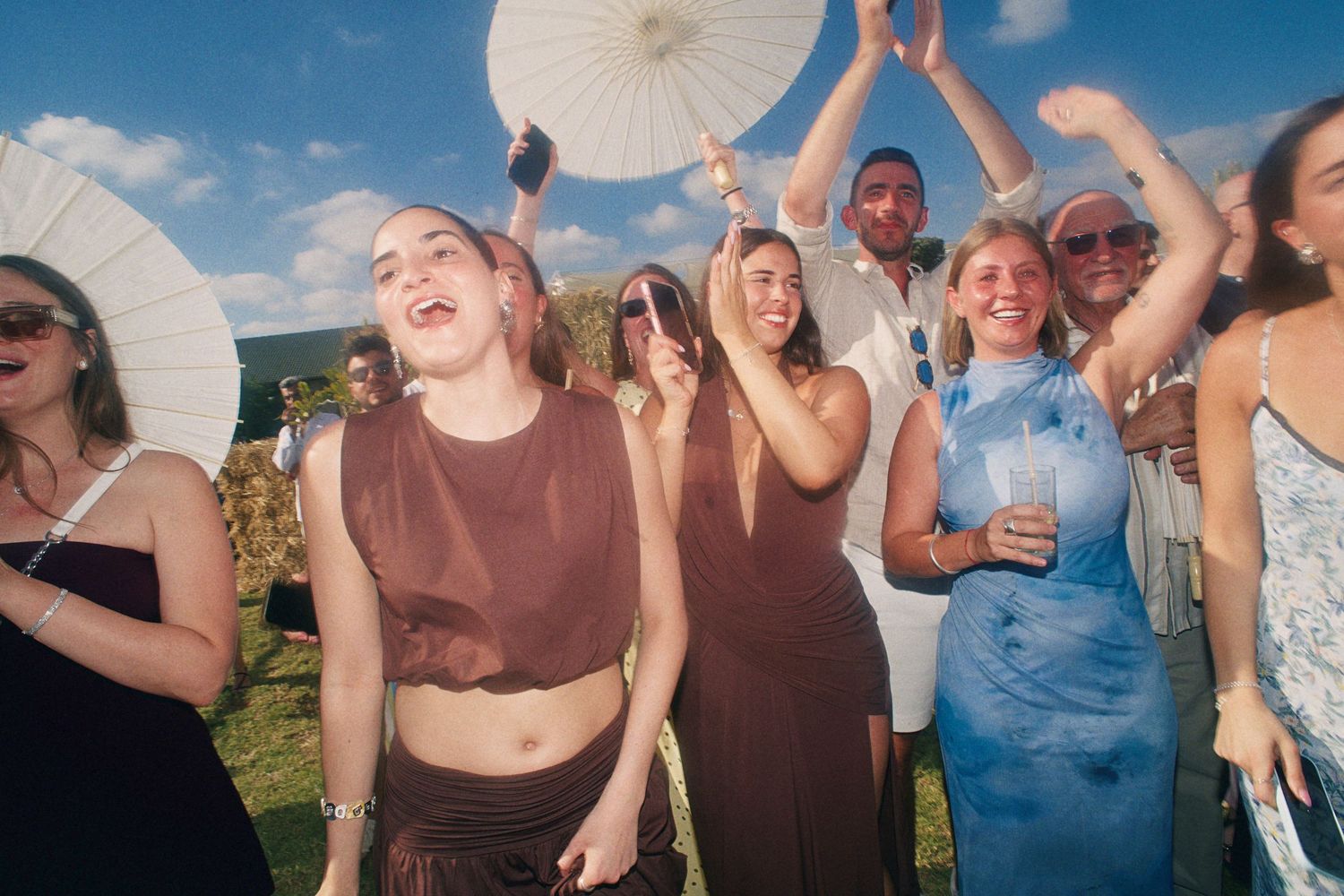 Joyful group of people dancing and celebrating outdoors at a sunny event.