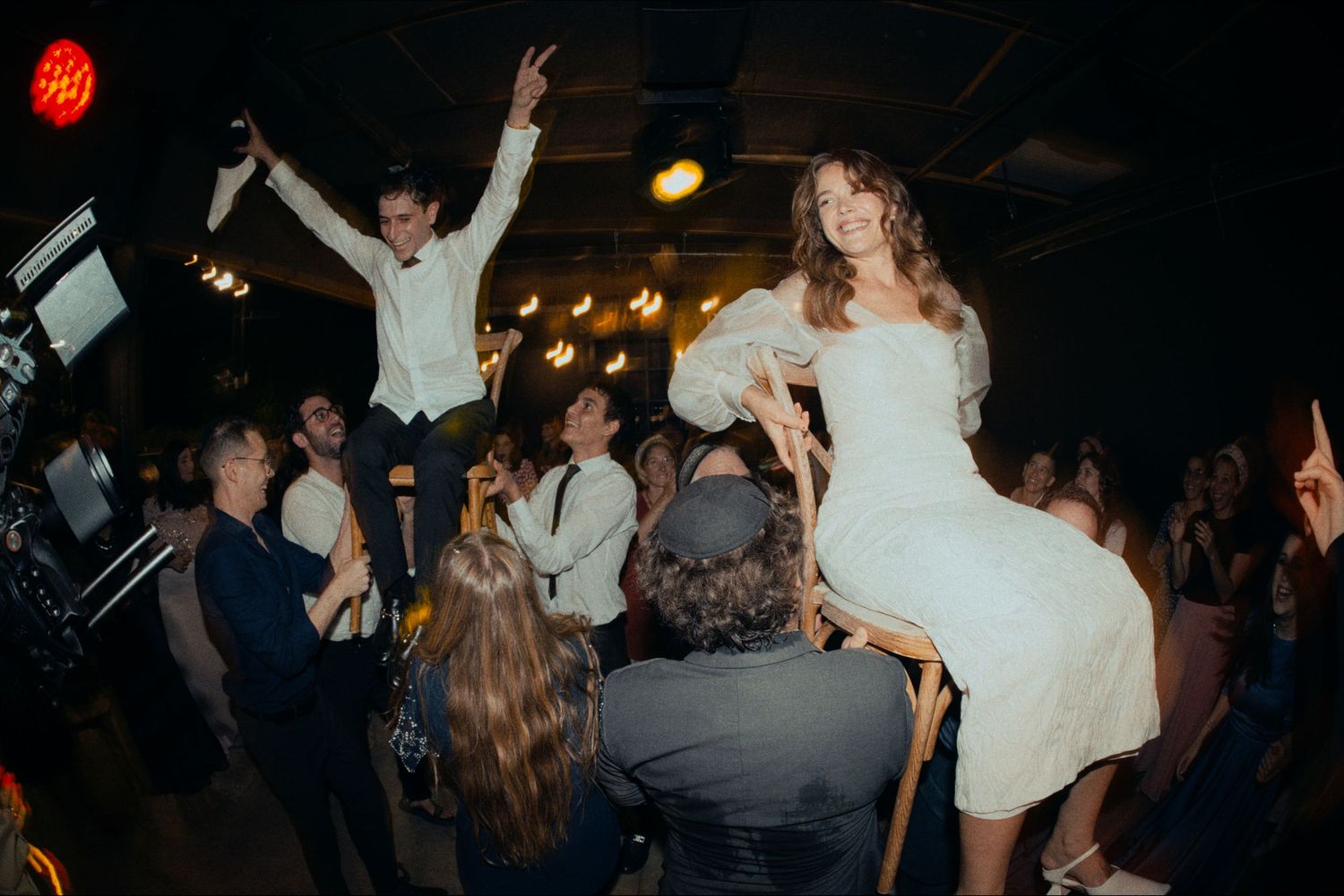 Wedding reception guests dance energetically under atmospheric lighting.