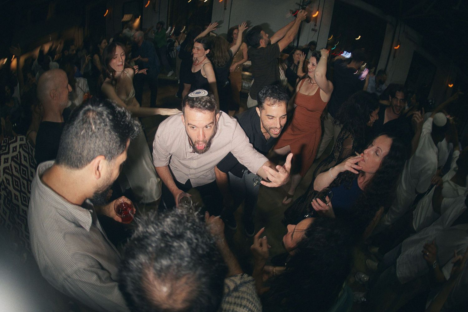 Crowd of wedding guests dancing closely together at a vibrant indoor wedding reception.
