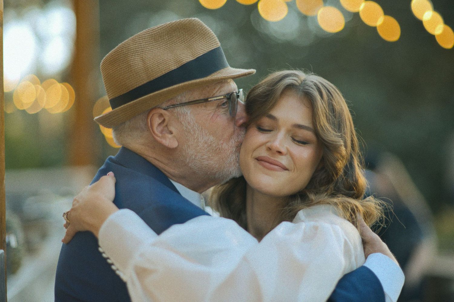 Romantic outdoor wedding moment captured at sunset with string lights in the background.