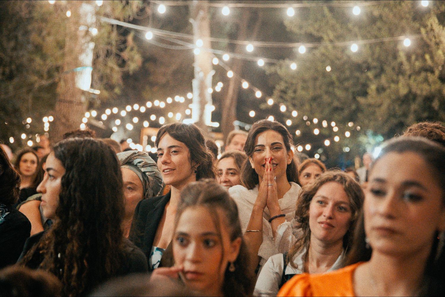 Wedding guests mingle under twinkling string lights at an outdoor evening reception.