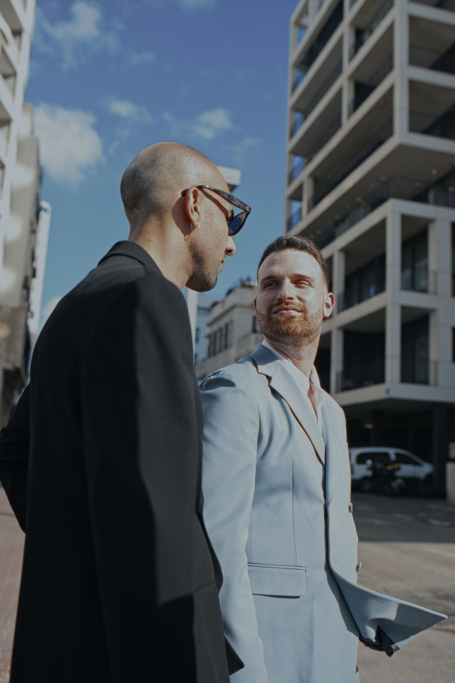 Gay couple in Tel Aviv- contrasting outfits having a conversation outside a modern building.