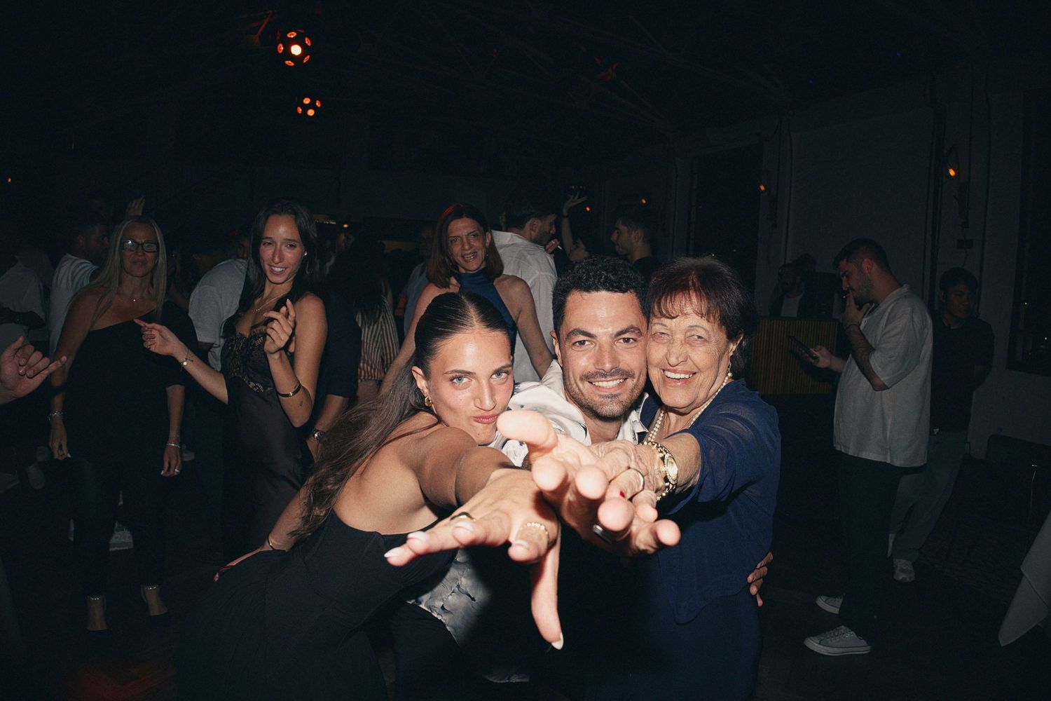 Three people pose and smile together on a lively dance floor at a nightclub party event.