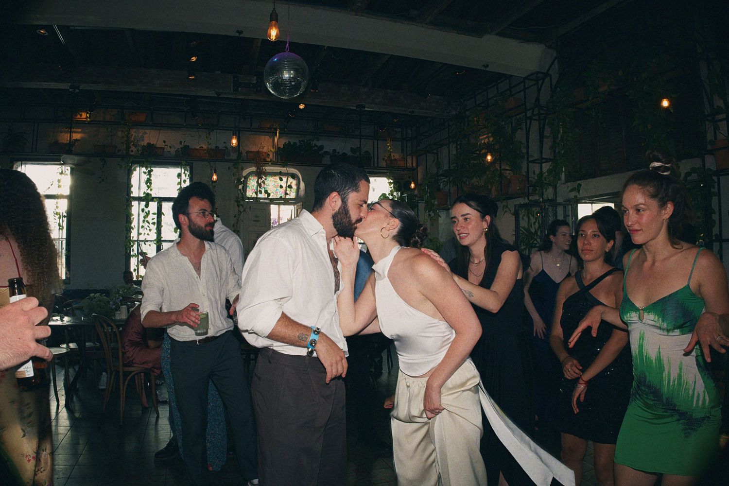 Bride and groom sharing a romantic kiss on the dance floor surrounded by wedding guests.