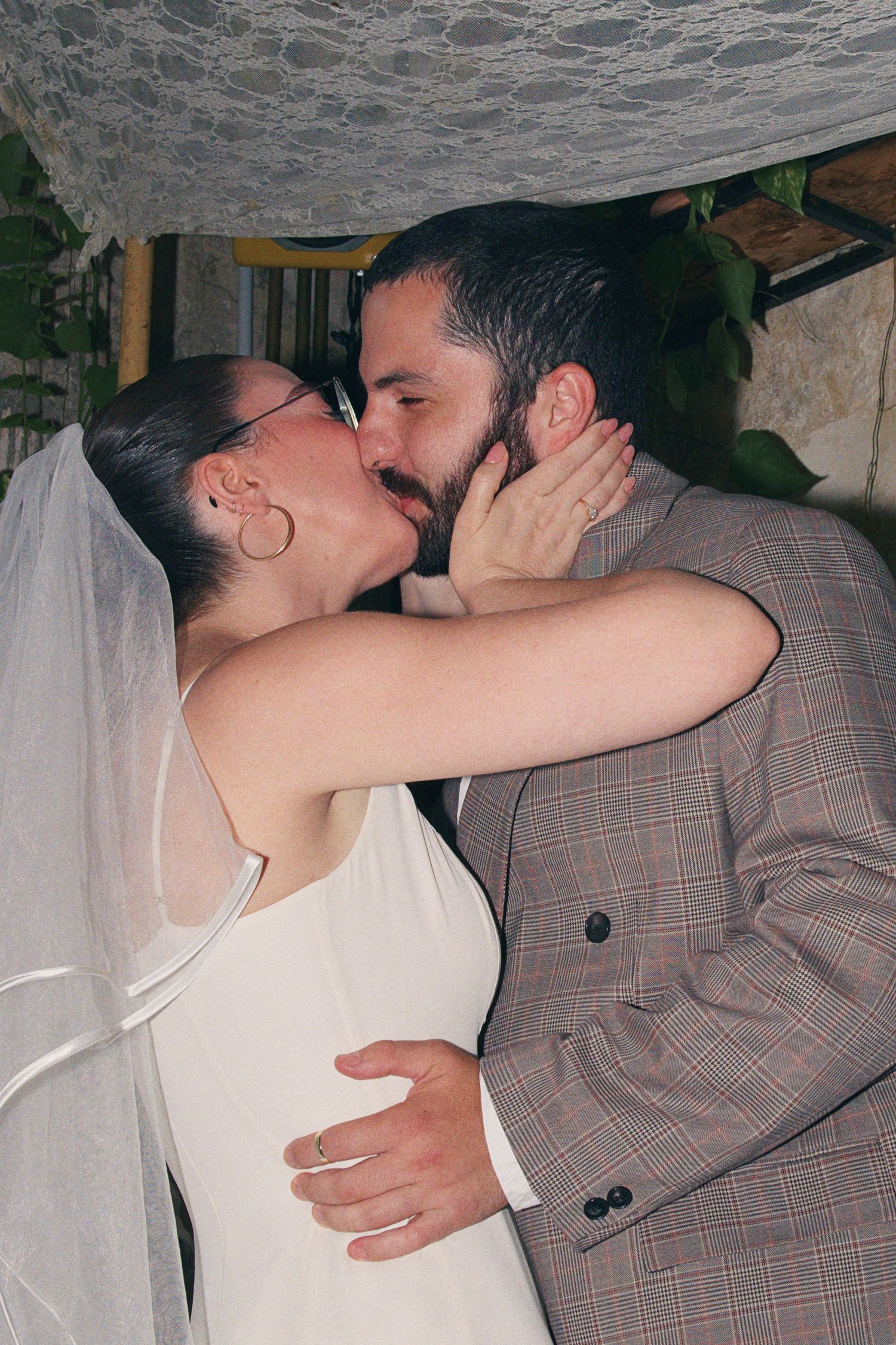 Bride and groom share first kiss under lace chuppah at Jewish wedding.