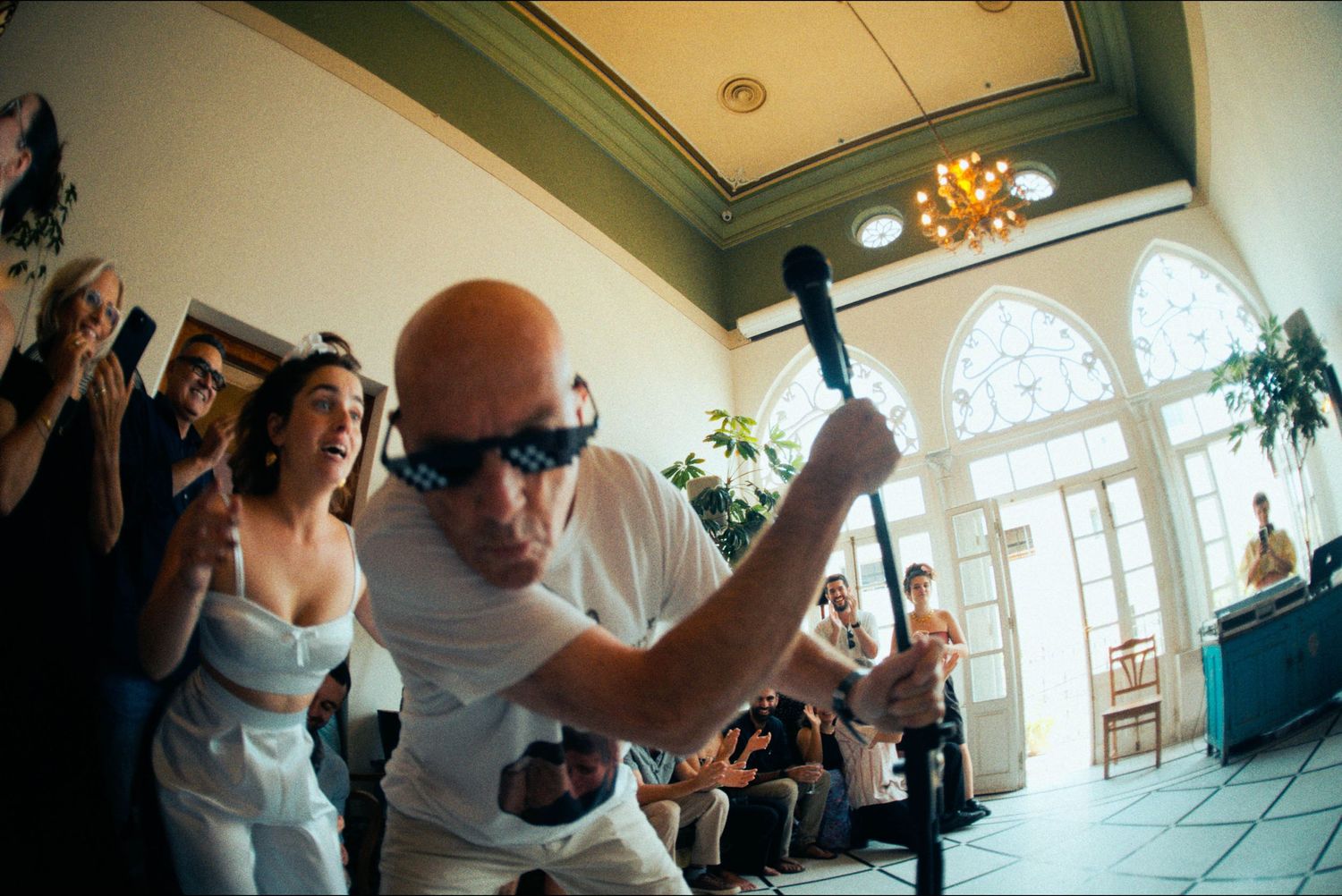 Wedding guests dance energetically at a lively reception party in an indoor venue.