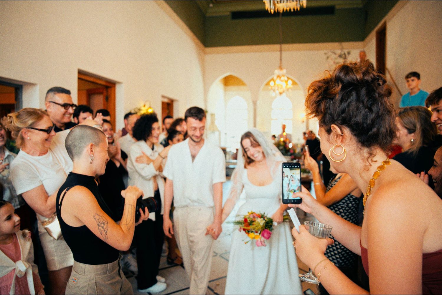 Wedding reception venue with guests mingling and celebrating under warm lighting.