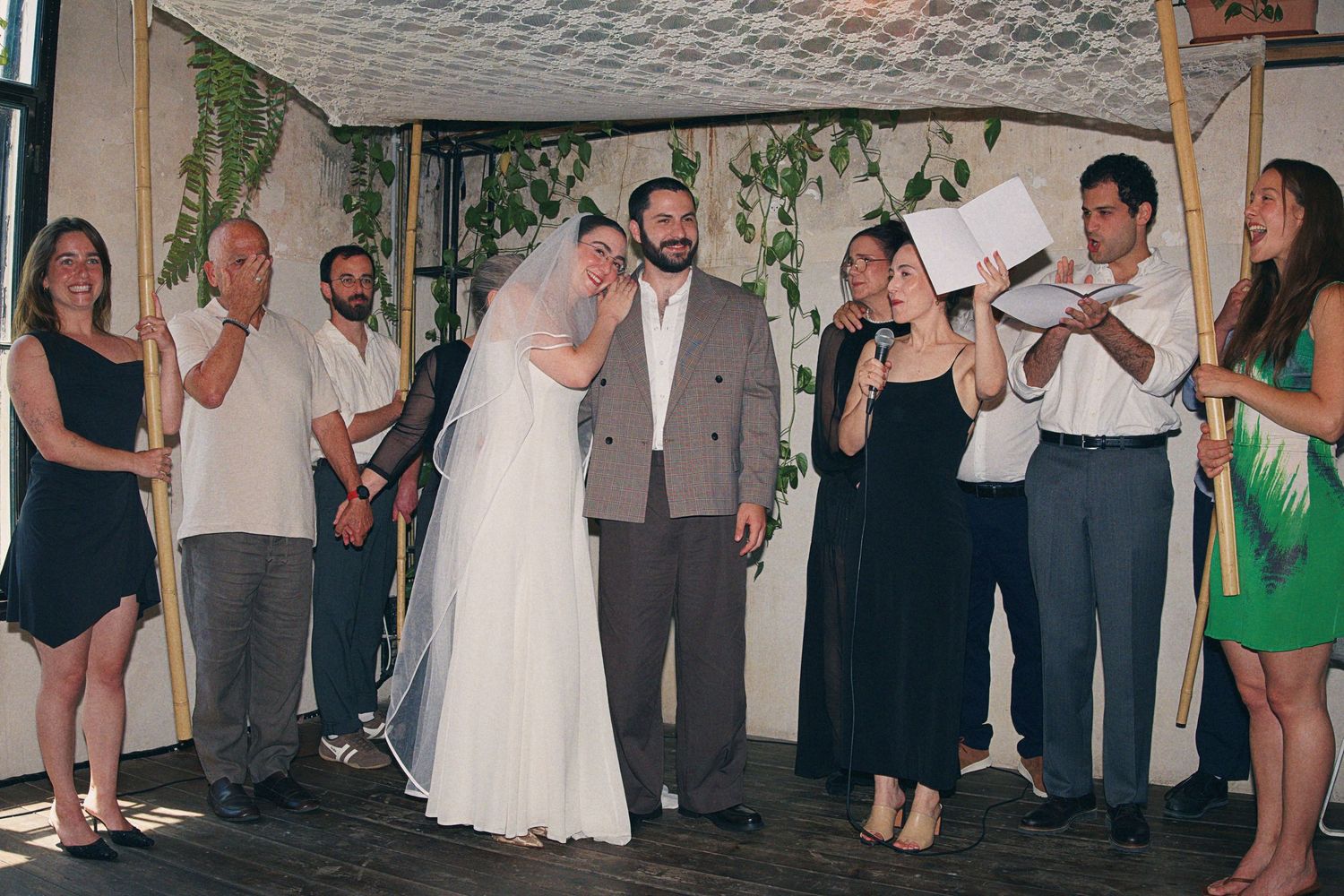 Bride and groom standing under a chuppah surrounded by wedding party guests during ceremony.