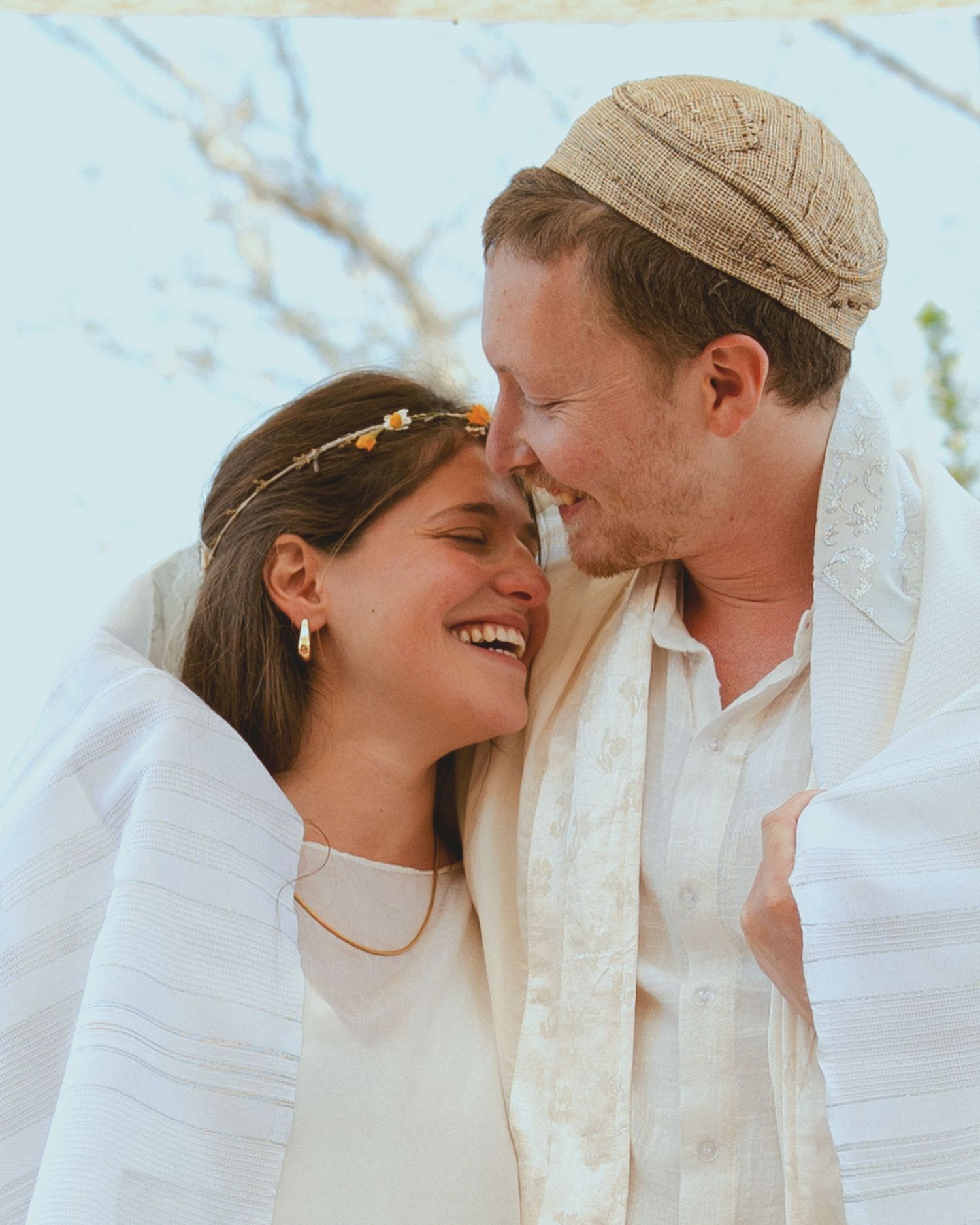A tender moment between a couple in white attire against a bright outdoor background.